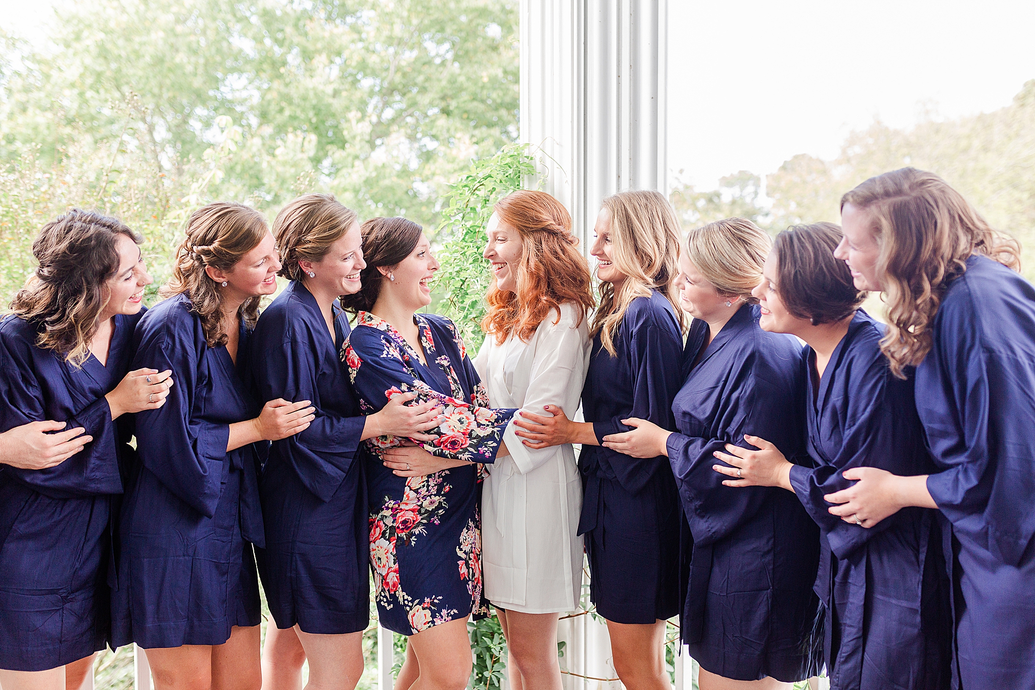 bride and bridesmaids in navy blue robes hug on patio