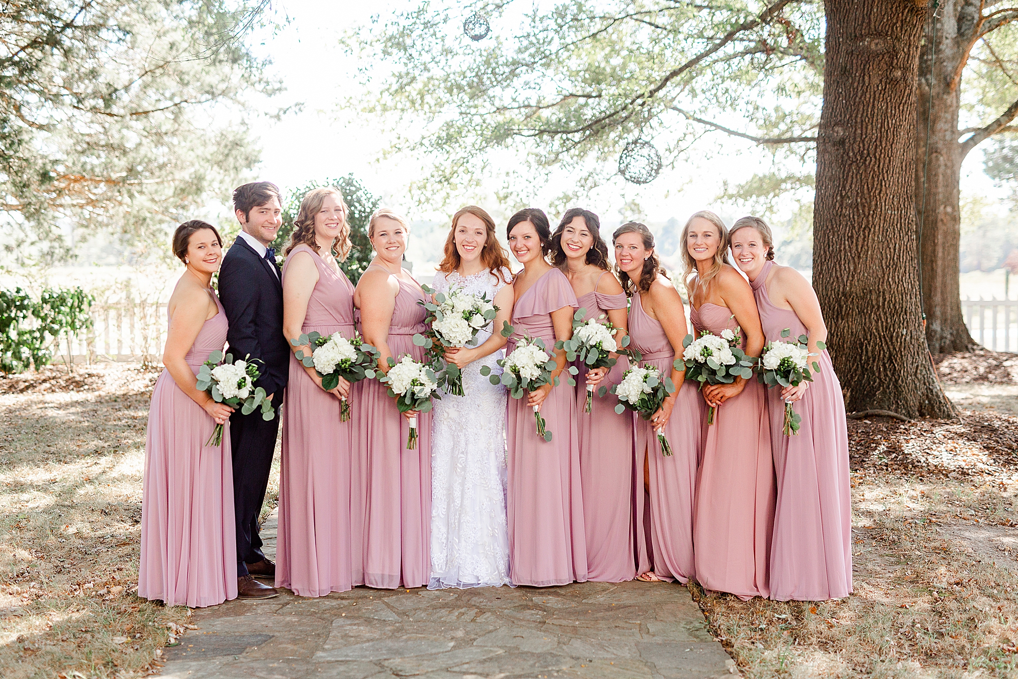 bride poses with bridesmaids and bridesman in pink gowns