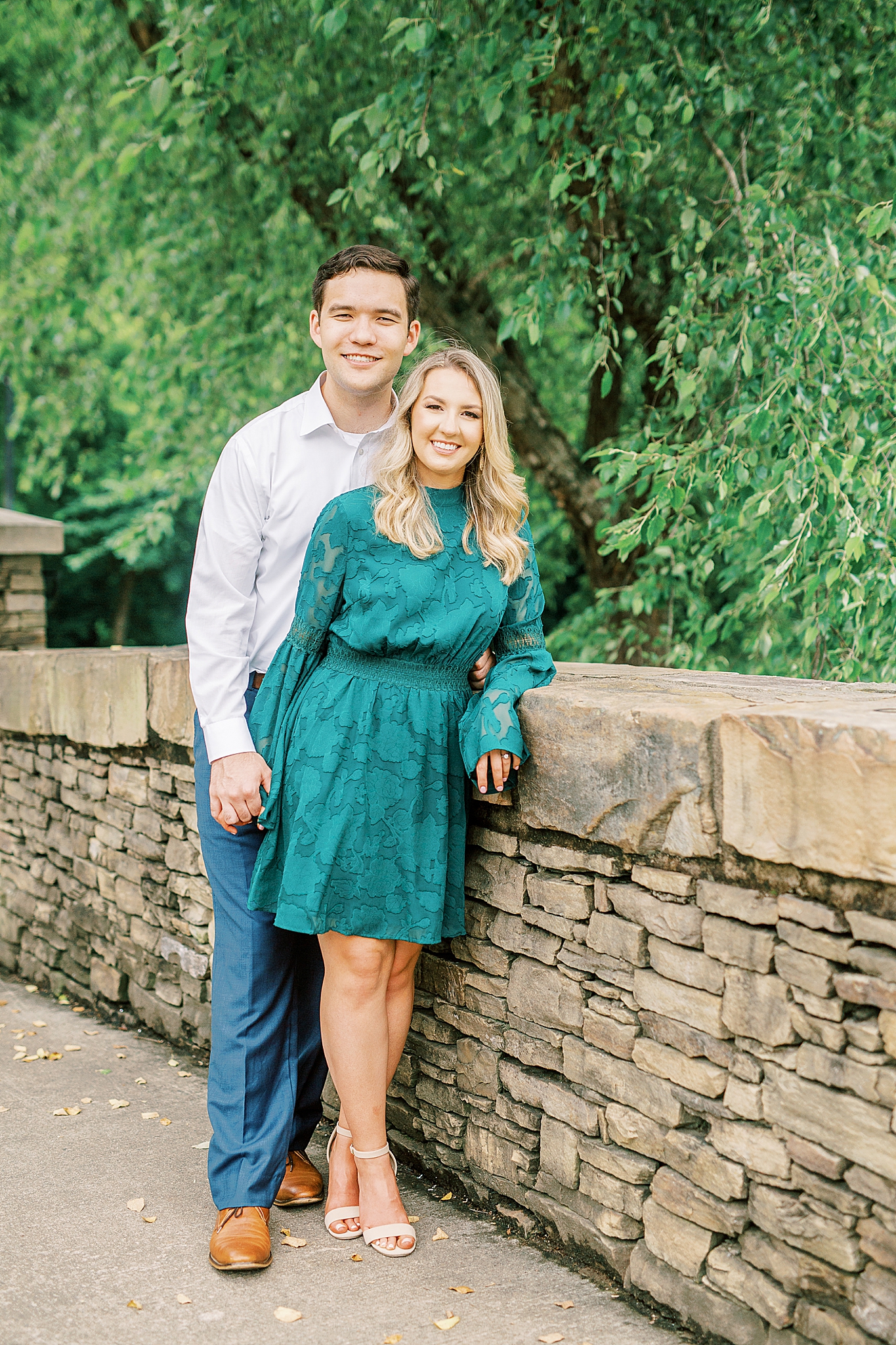 uptown Charlotte engagement session with couple leaning against stone wall