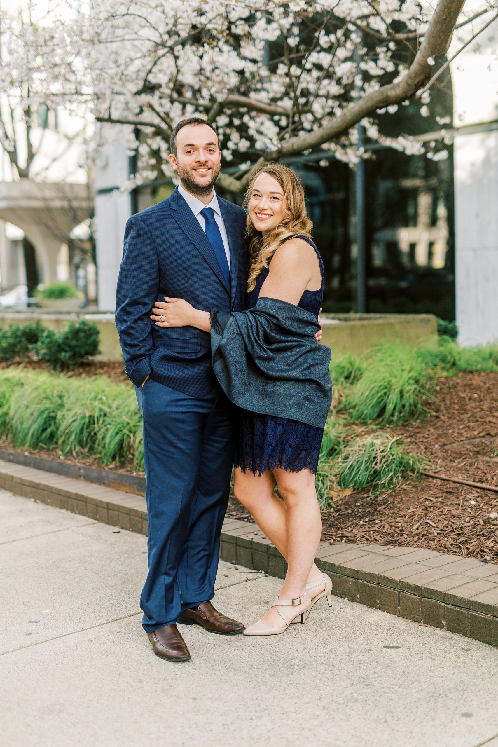 bride wearing navy wrap and dress hugs groom in navy suit standing in Uptown Charlotte