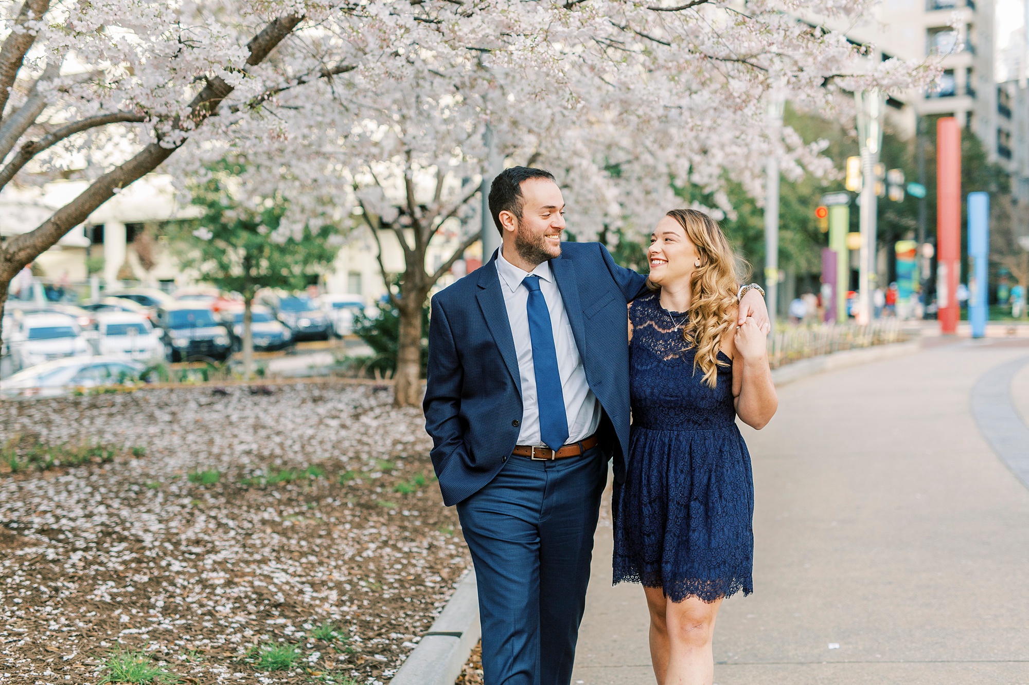 engaged couple walks along pink trees in Uptown Charlotte