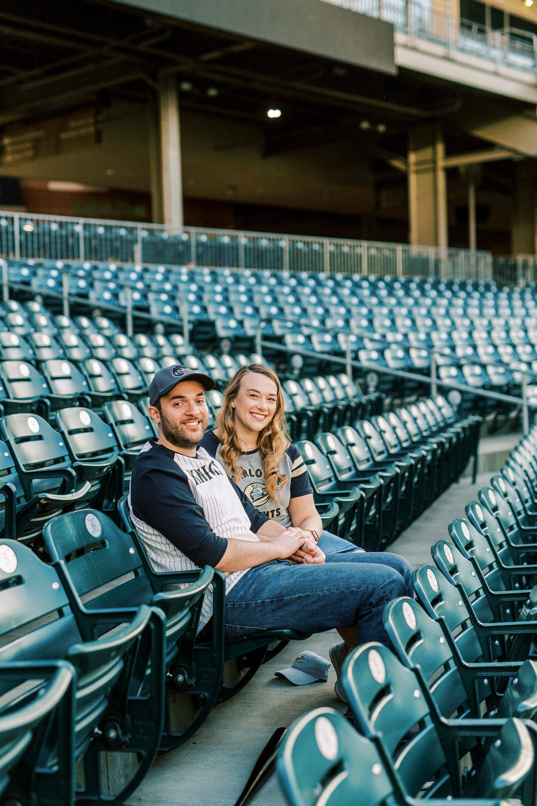 couple sits on bench at Truist Field during engagement photos