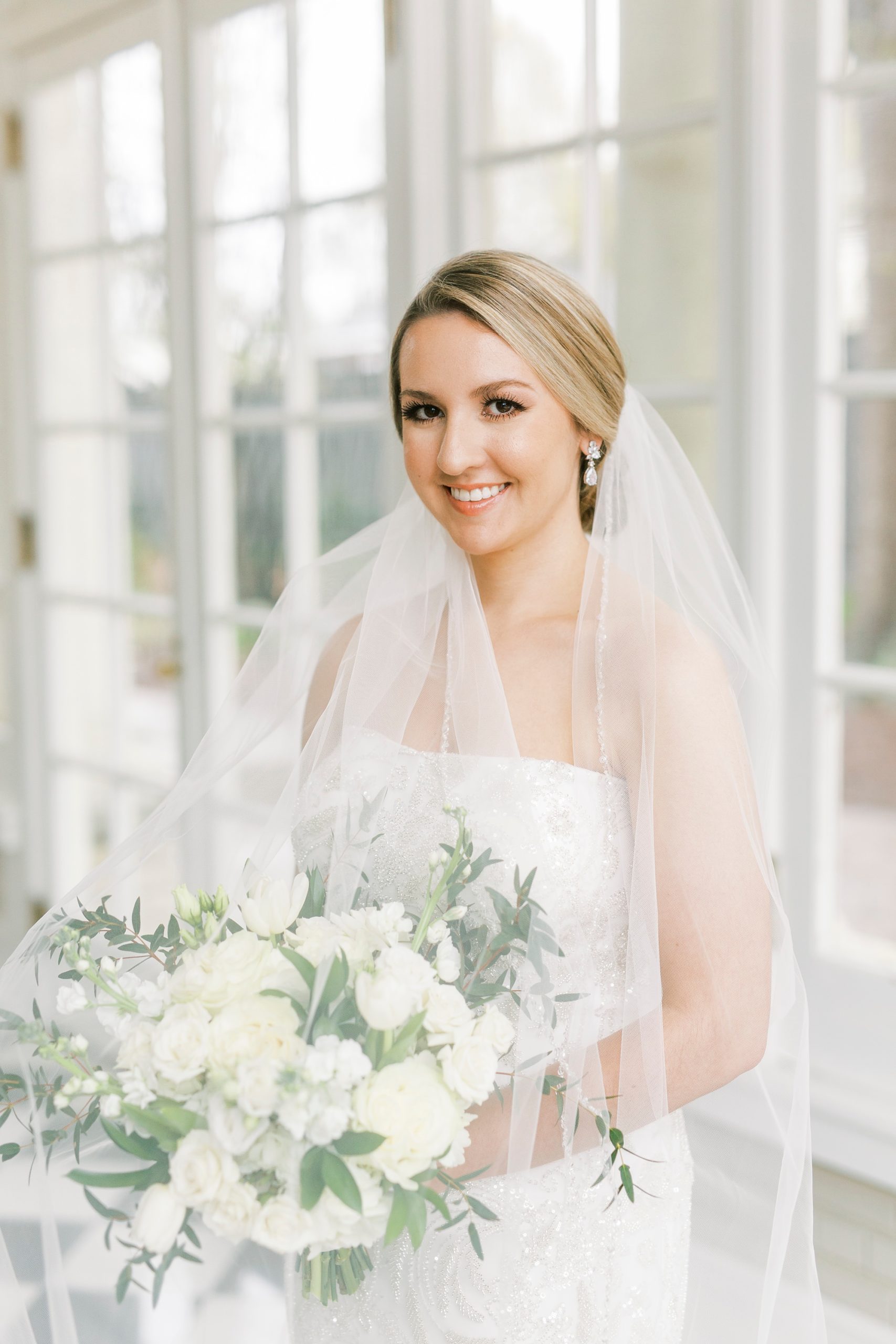 bride holds bouquet of ivory flowers under cathedral veil