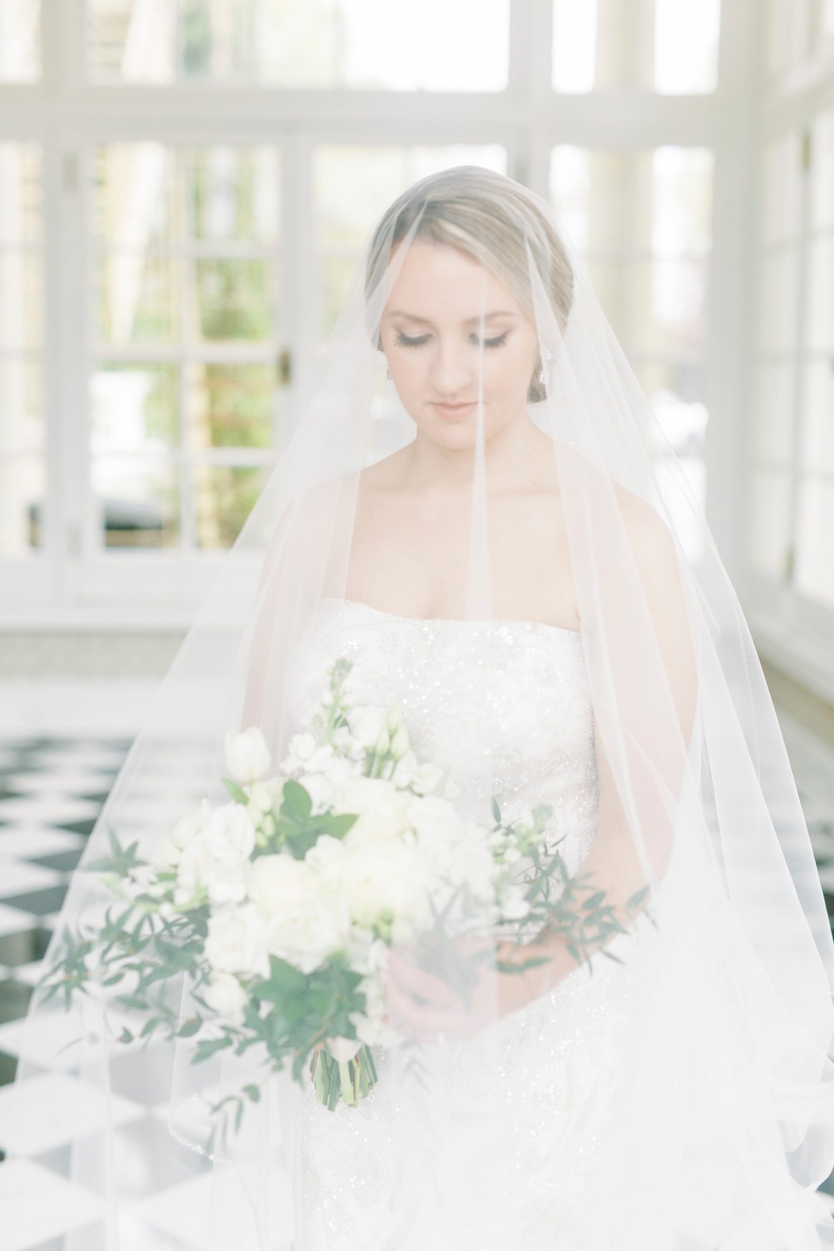 bride looks at ivory bouquet under cathedral veil