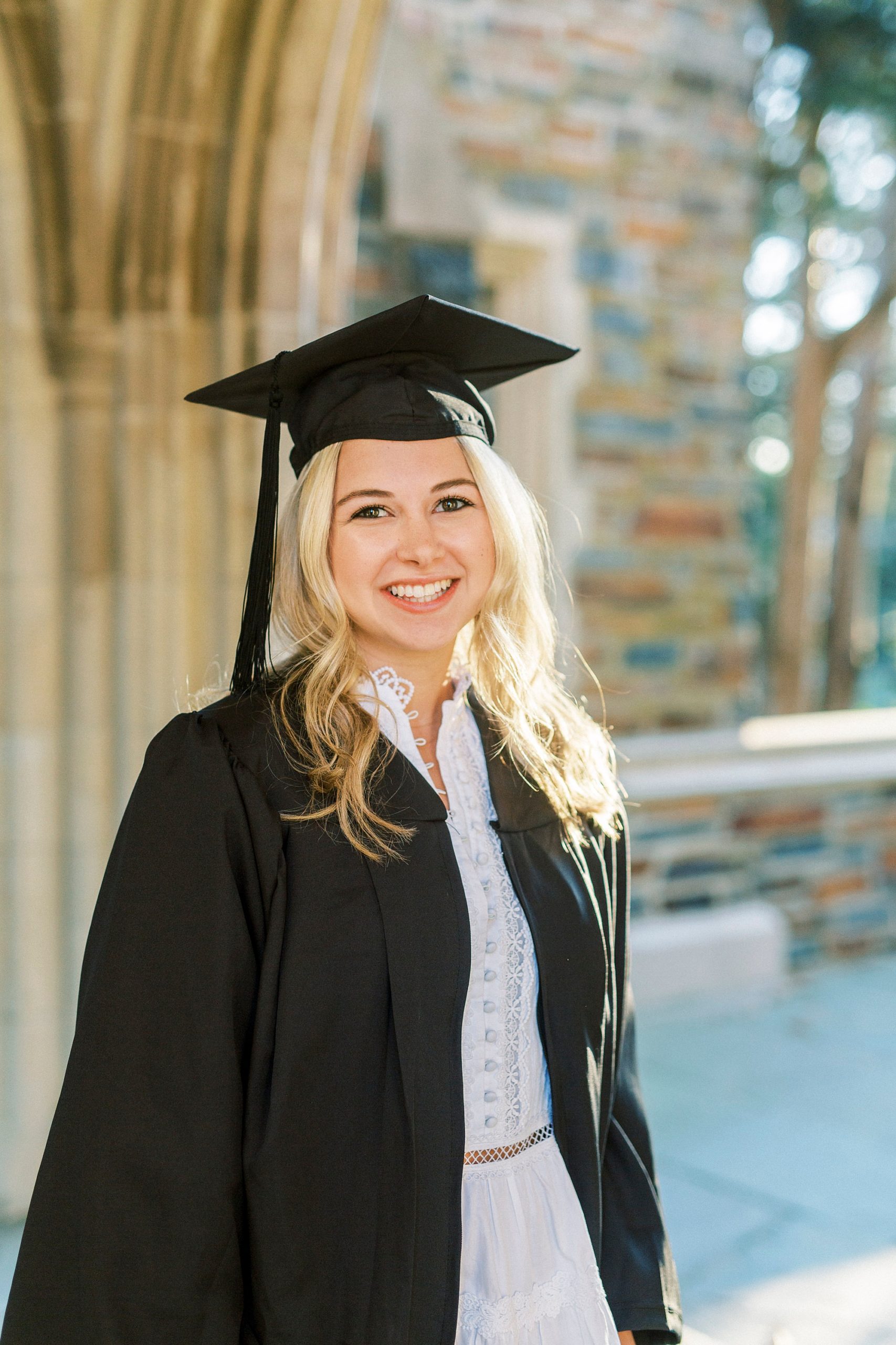 student in cap and gown poses by archway at Duke Chapel