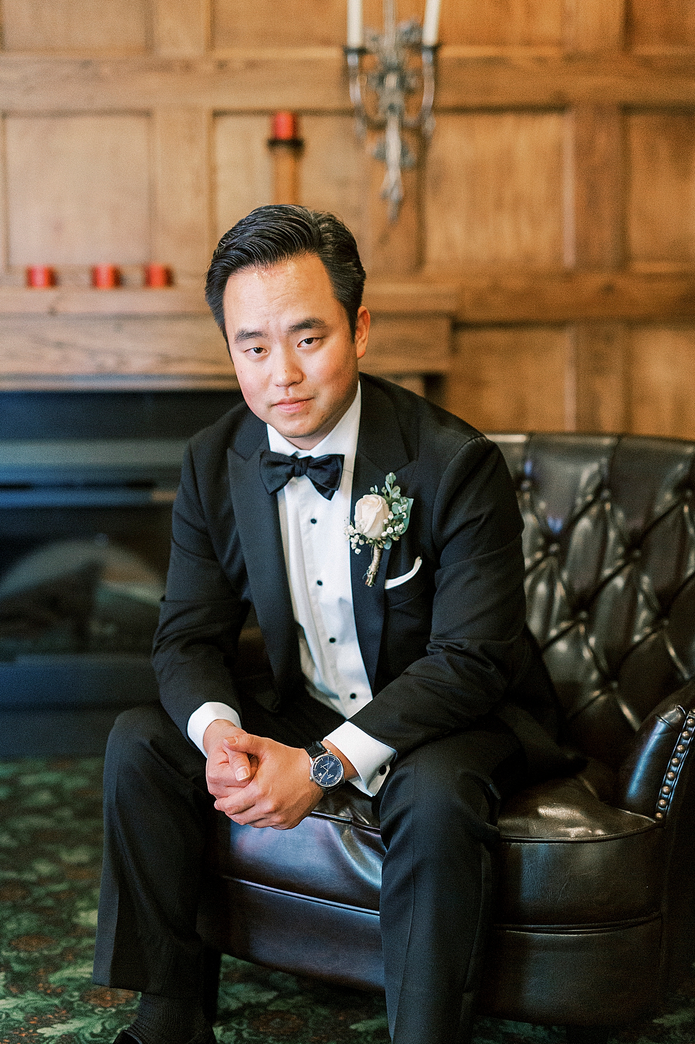 groom sits on leather couch in wood paneled room