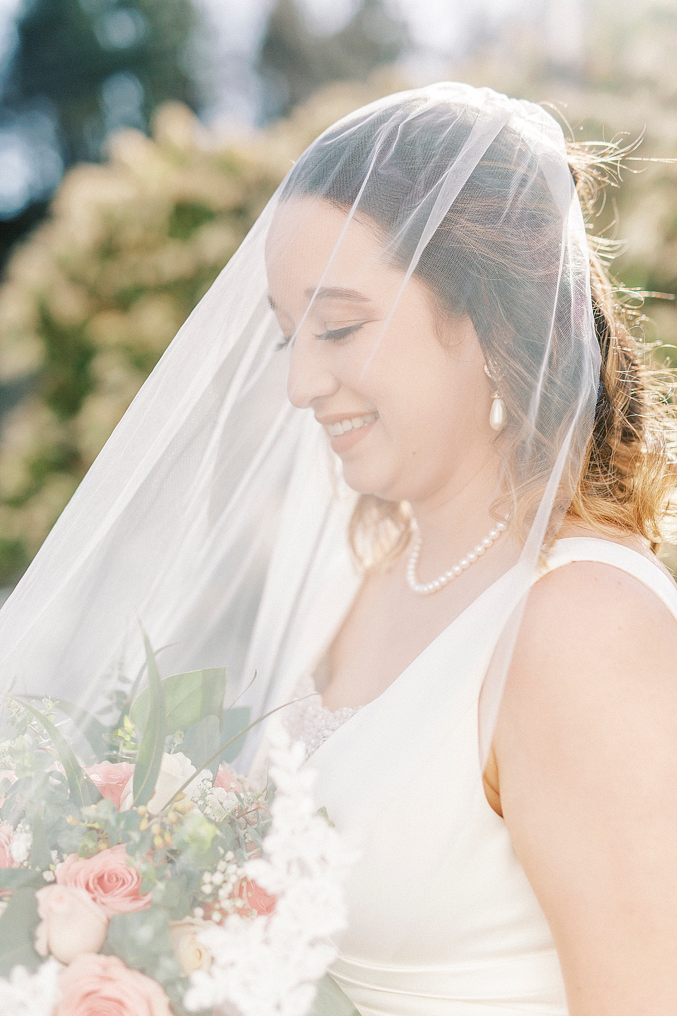 bride looks down at bouquet under veil