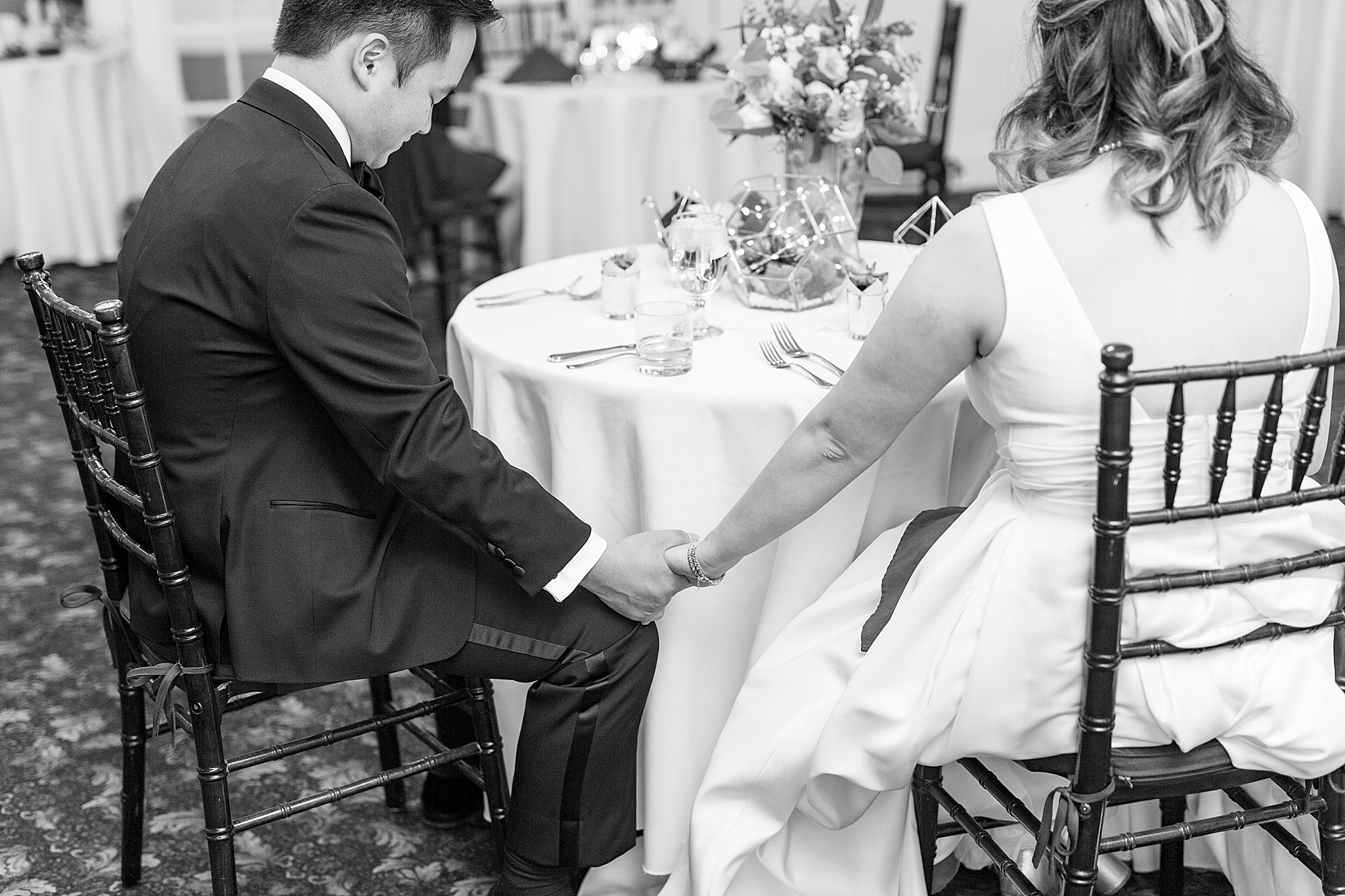 newlyweds hold hands listening to toasts