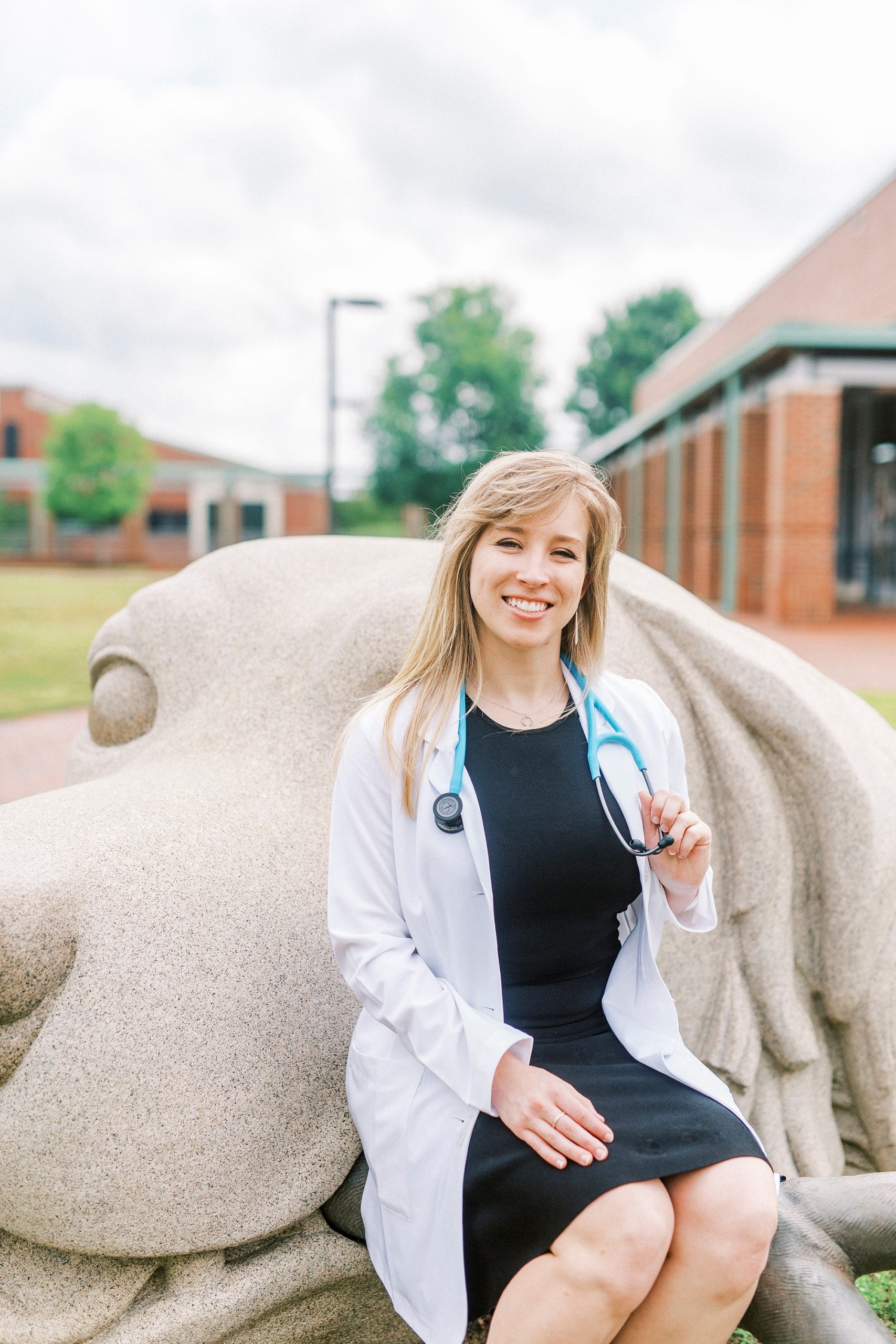 graduate in white lab coat poses by dog statue at NCSU