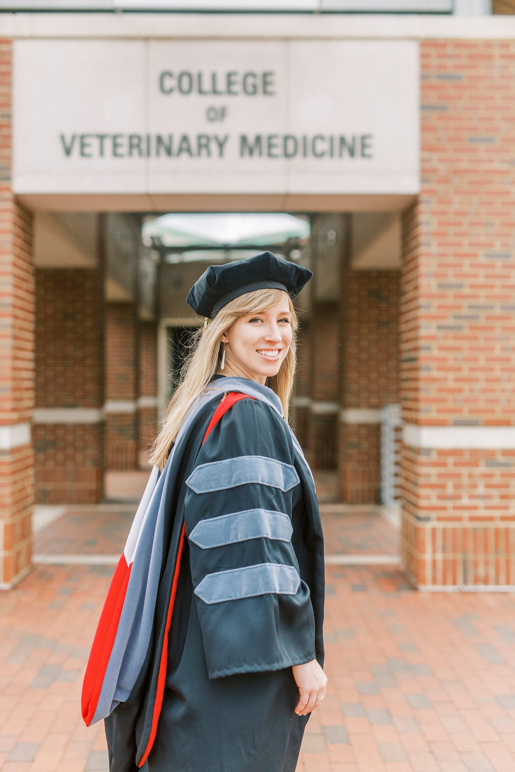 graduate wearing cap and gown looks over shoulder during NC State Vet School senior portraits