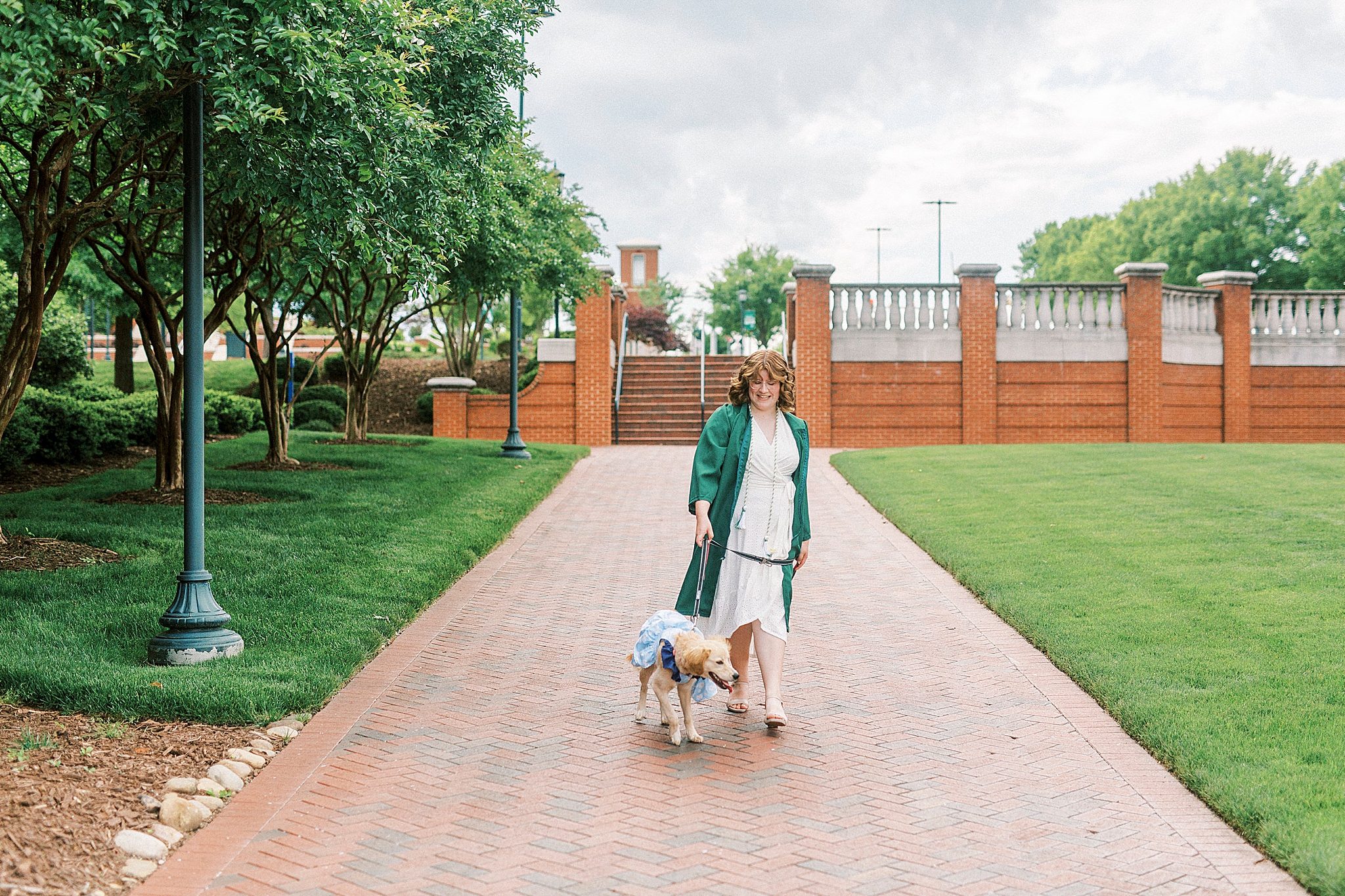 graduate in green robe walks dog on Charlotte college campus