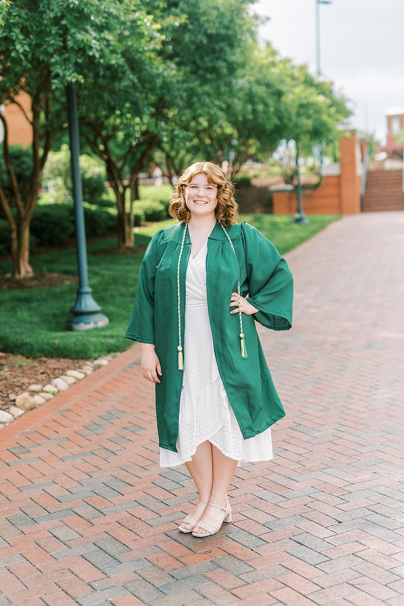 college graduate in green robe poses on UNCC campus