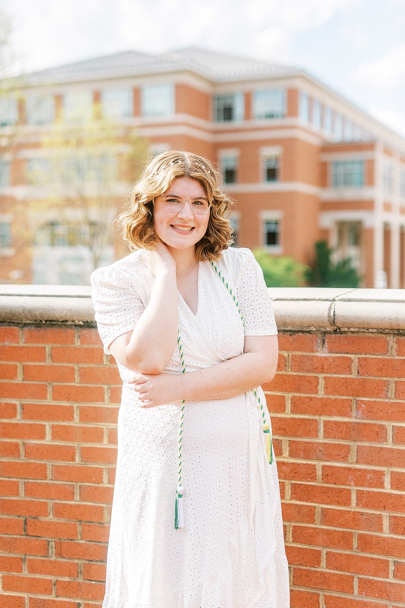 college graduate poses in white dress by UNCC campus