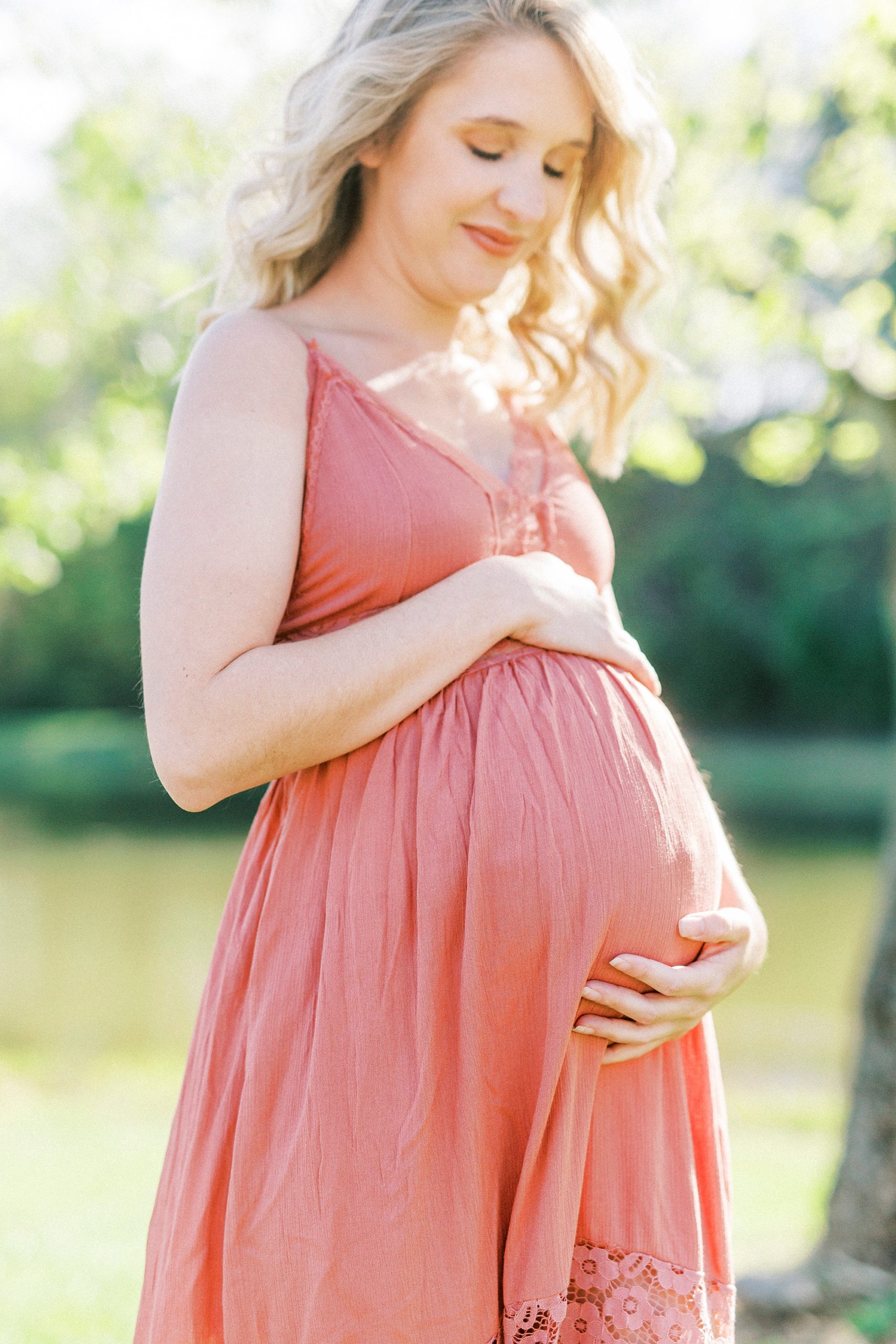 expecting mother holds belly in pink sundress and looks down