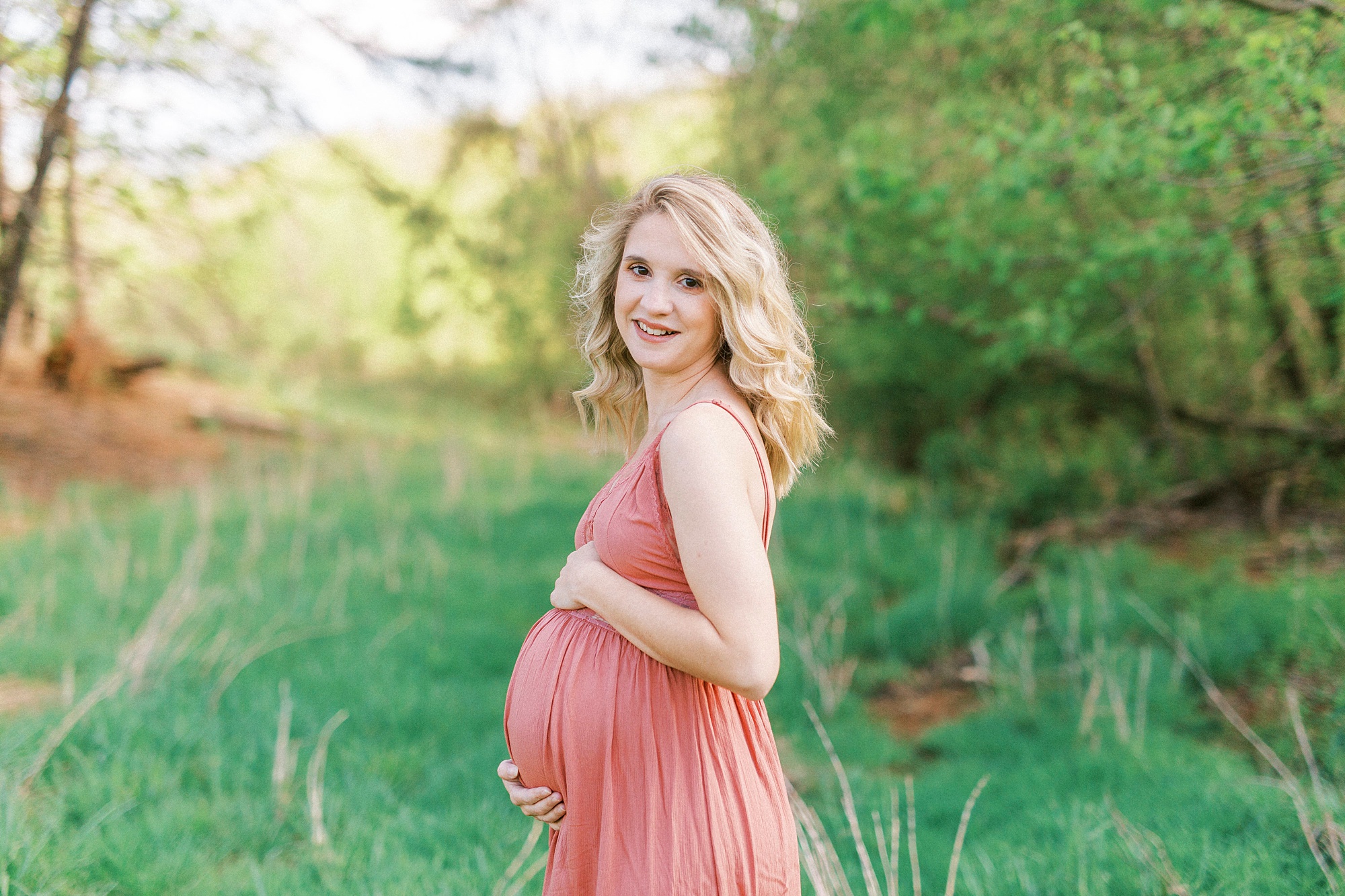 woman in pink sundress holds round belly during Mount Airy maternity photos