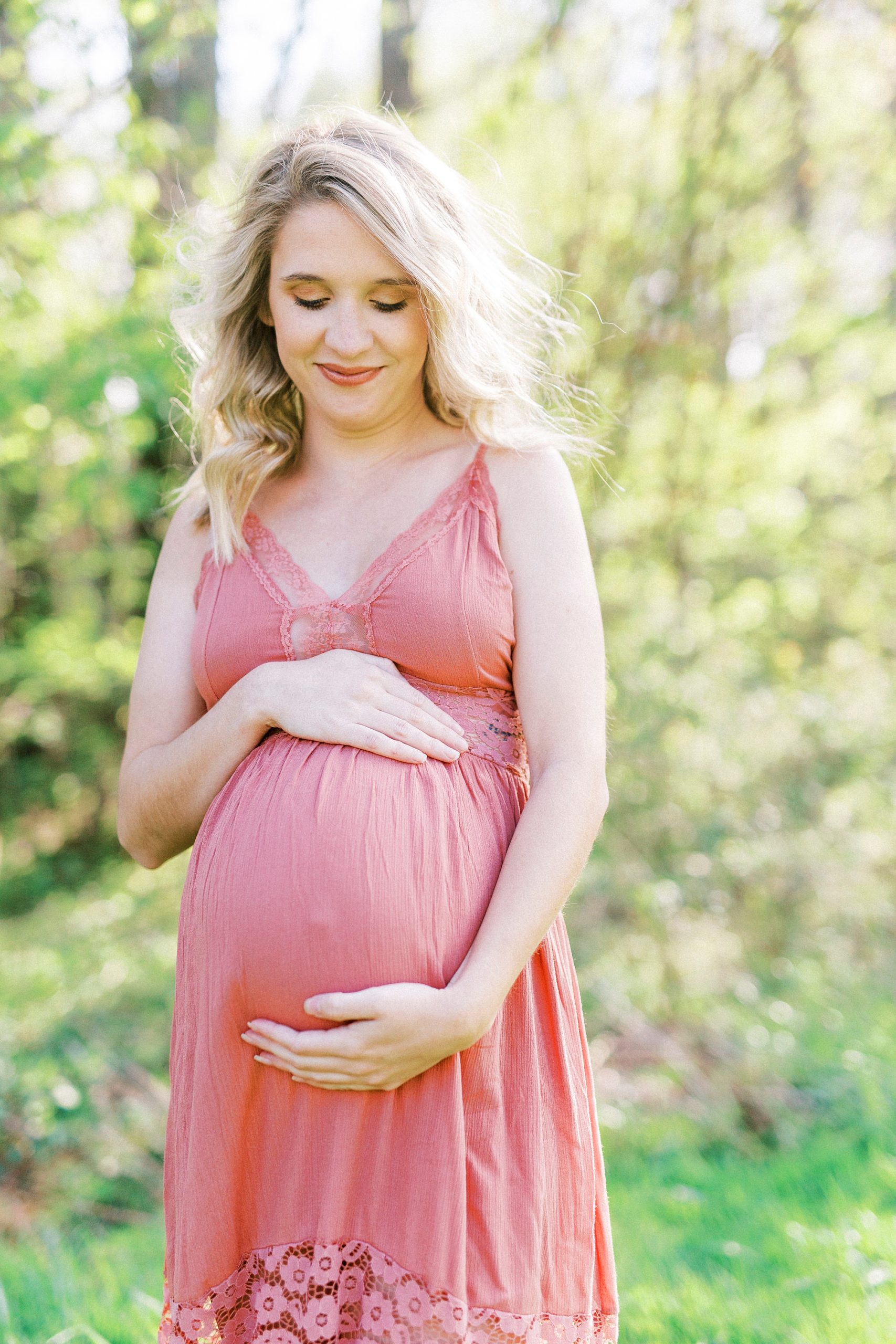 mother in pink gown holds belly during Winston-Salem maternity photos