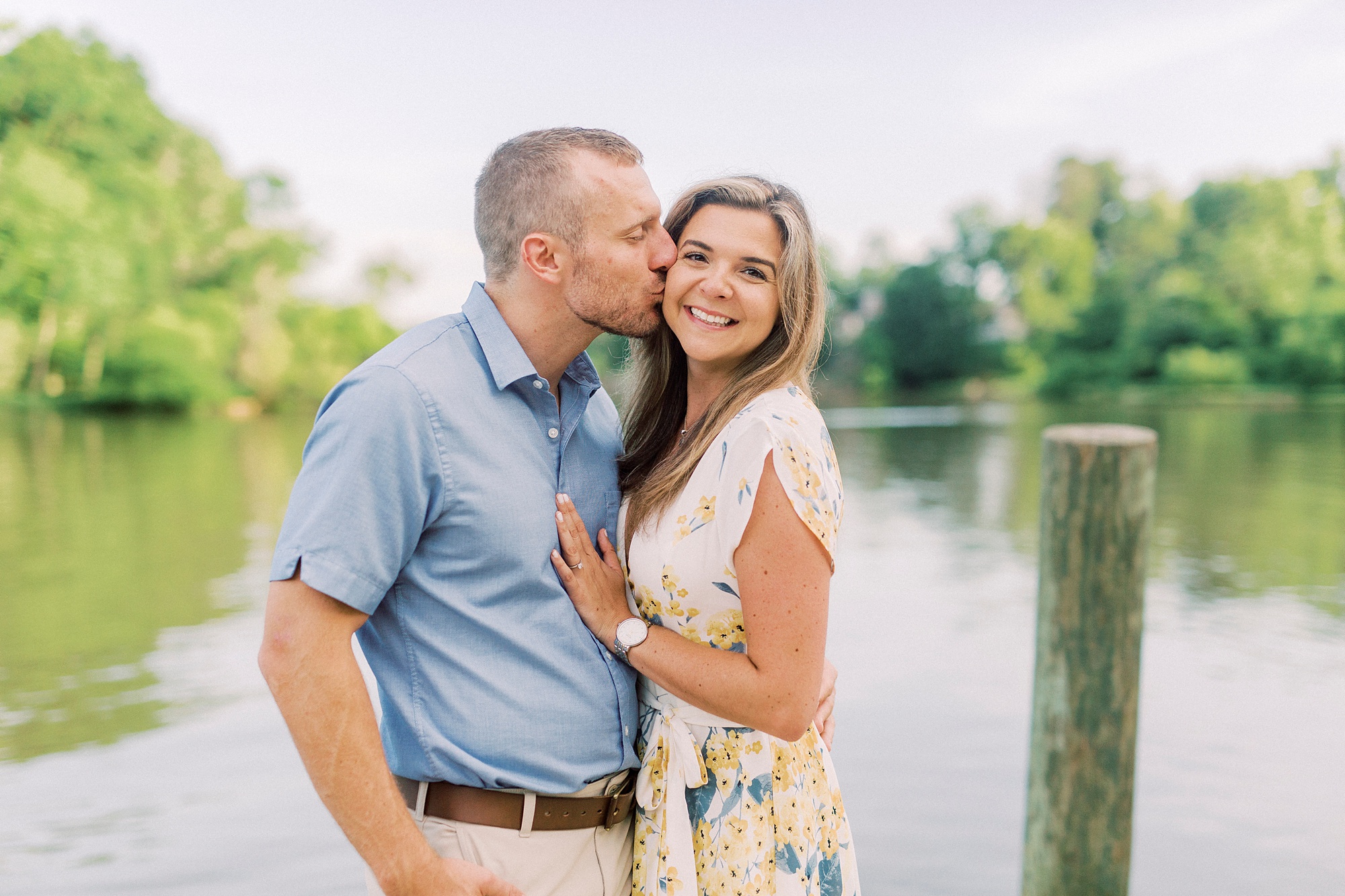 groom kisses bride's cheek during Downtown Belmont engagement photos along water