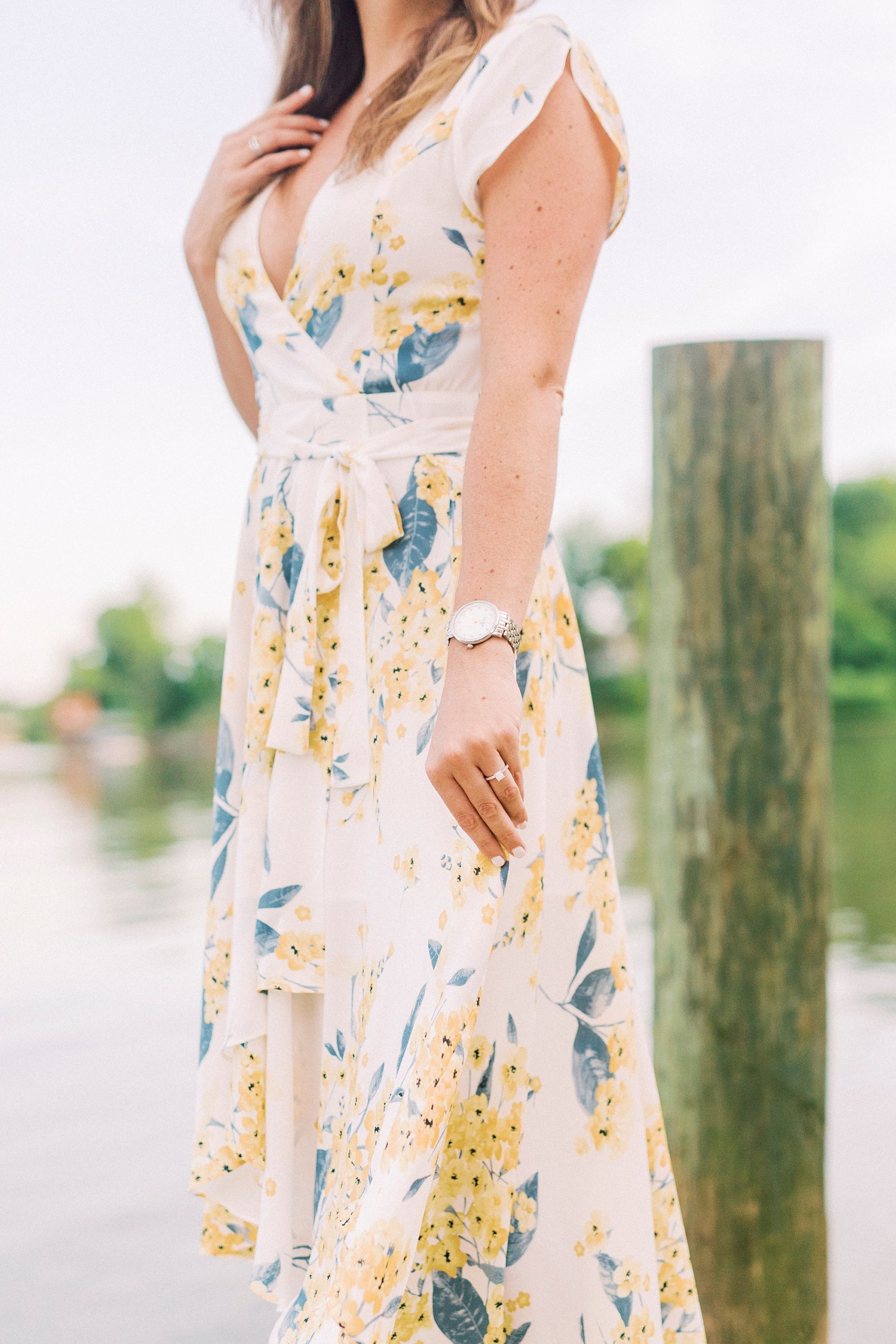 bride holds floral dress with left hand on pier