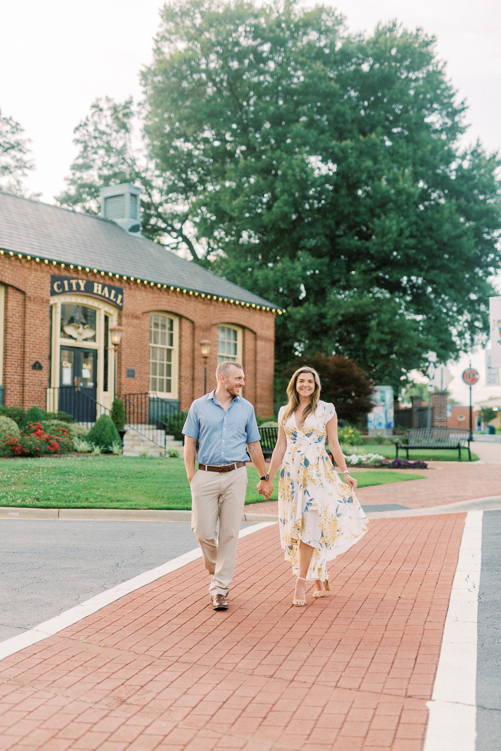 engaged couple walks by City hall in Downtown Belmont