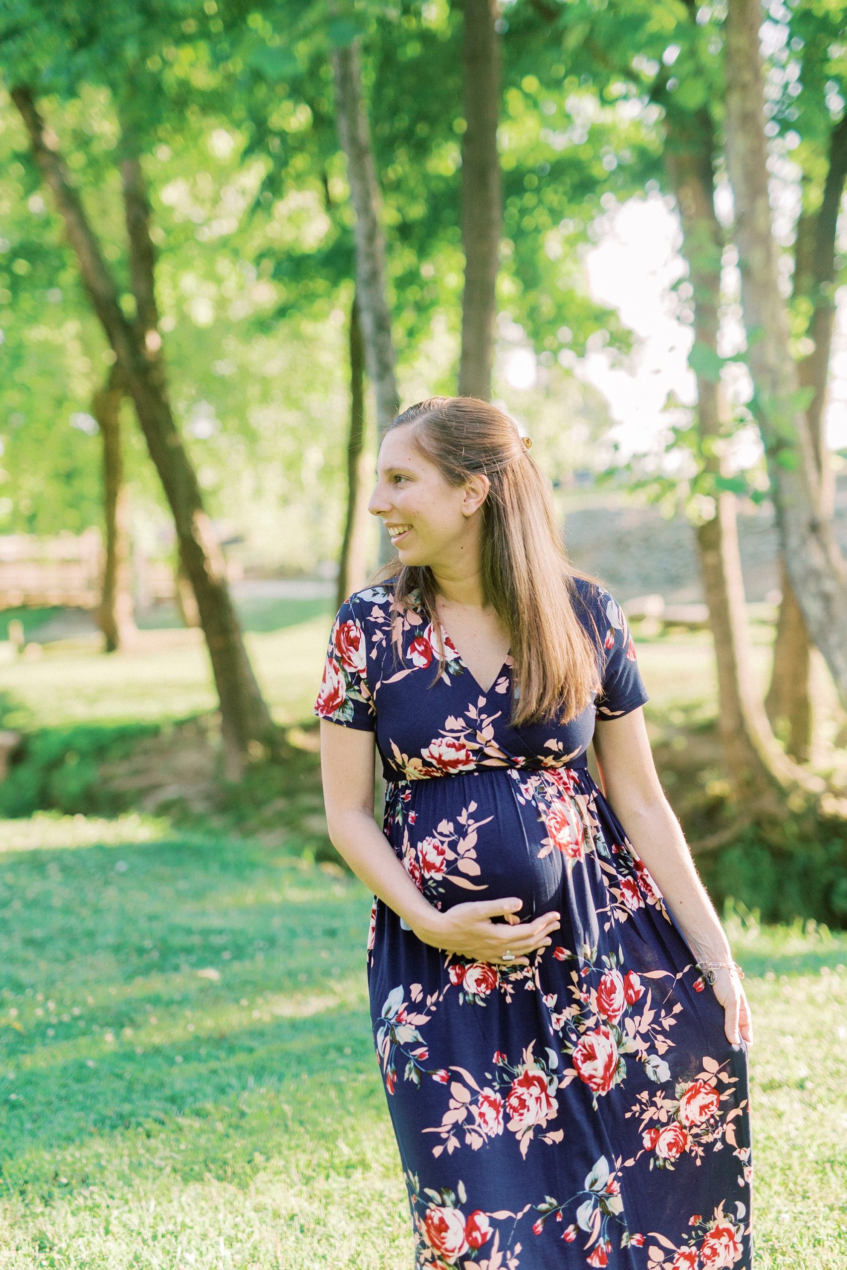 woman holds belly and edge of skirt looking over shoulder during Rankin Lake Park maternity session