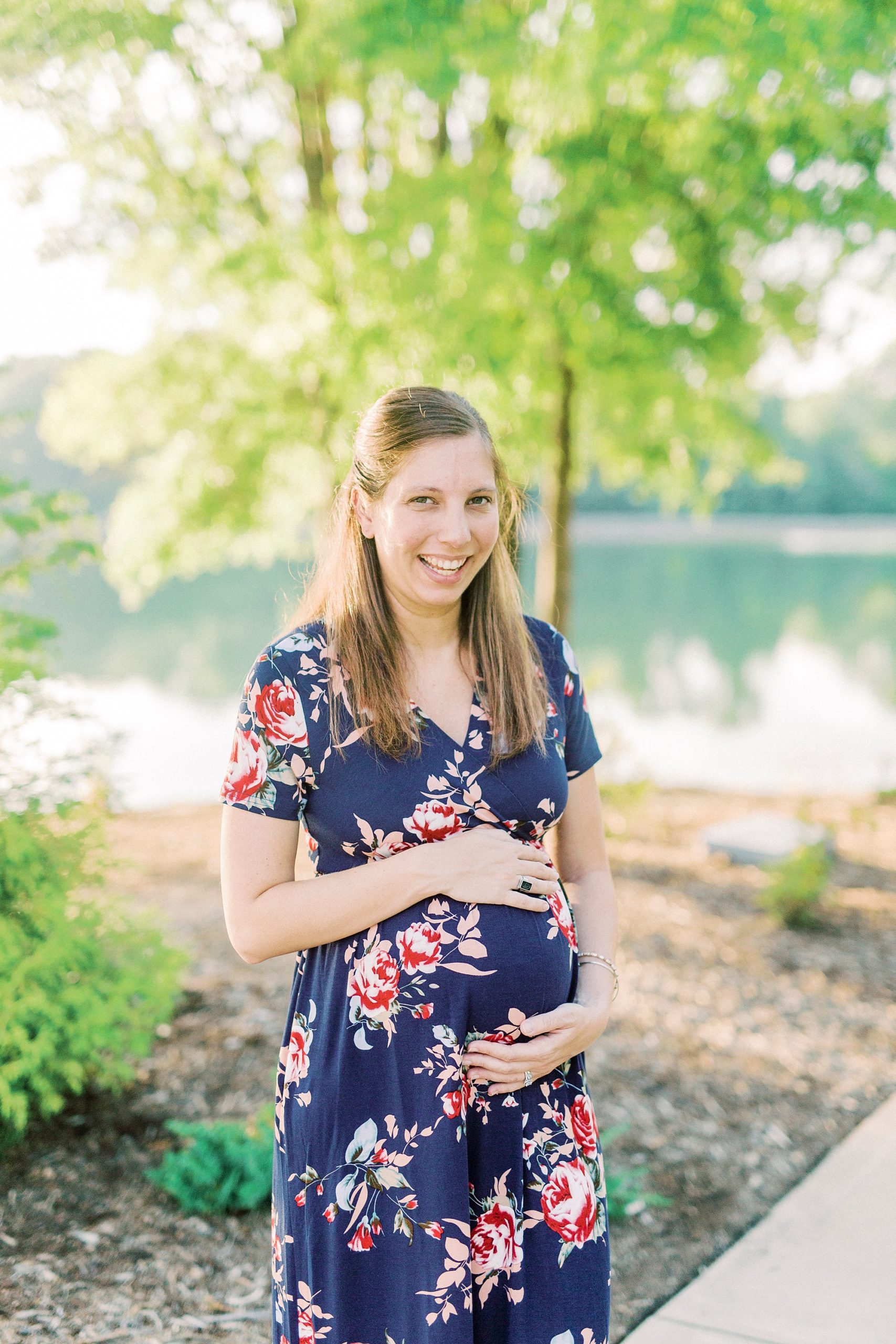 woman holds belly in blue dress during maternity photos in NC