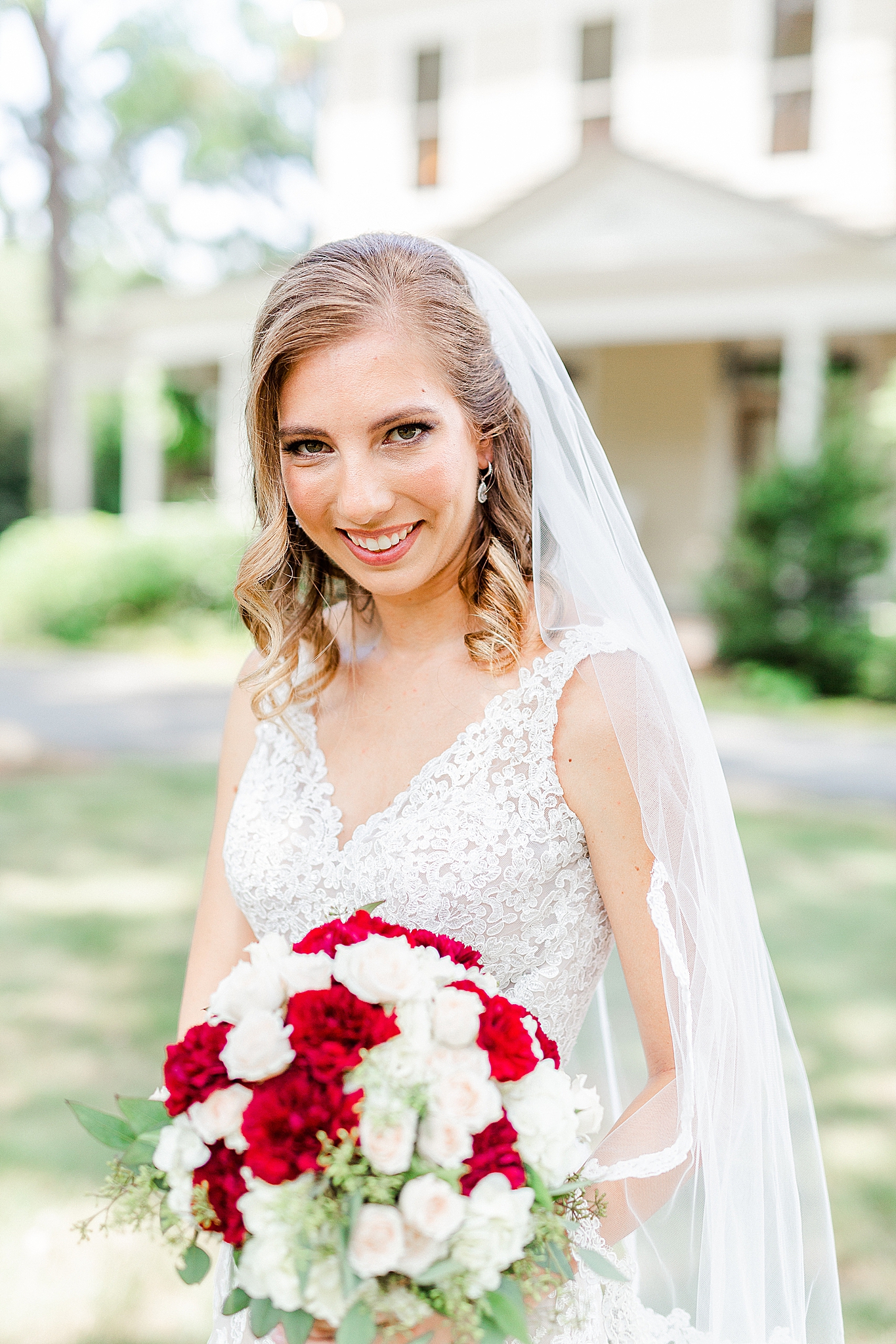 bride smiles holding bouquet of white and red flowers during Alexander Homestead bridal portraits