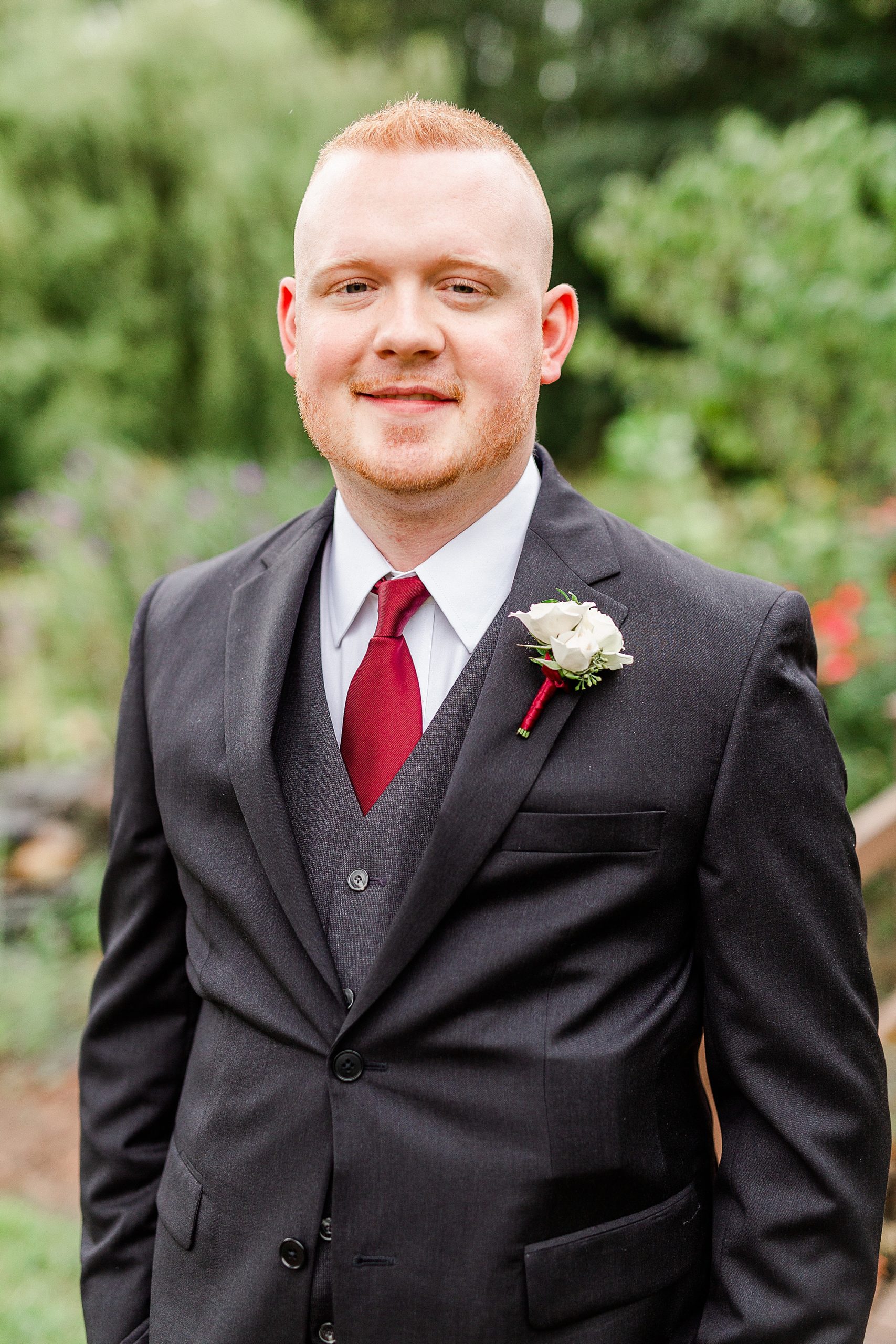 groom in black suit with red tie smiles at Alexander Homestead