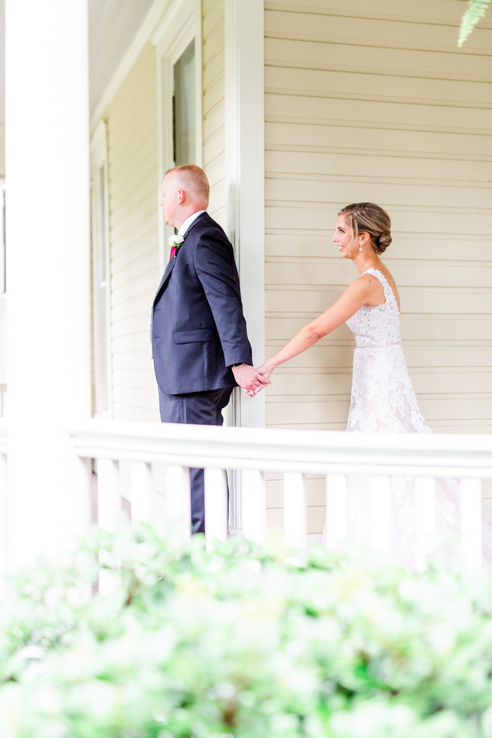bride holds groom's hand on porch during first look