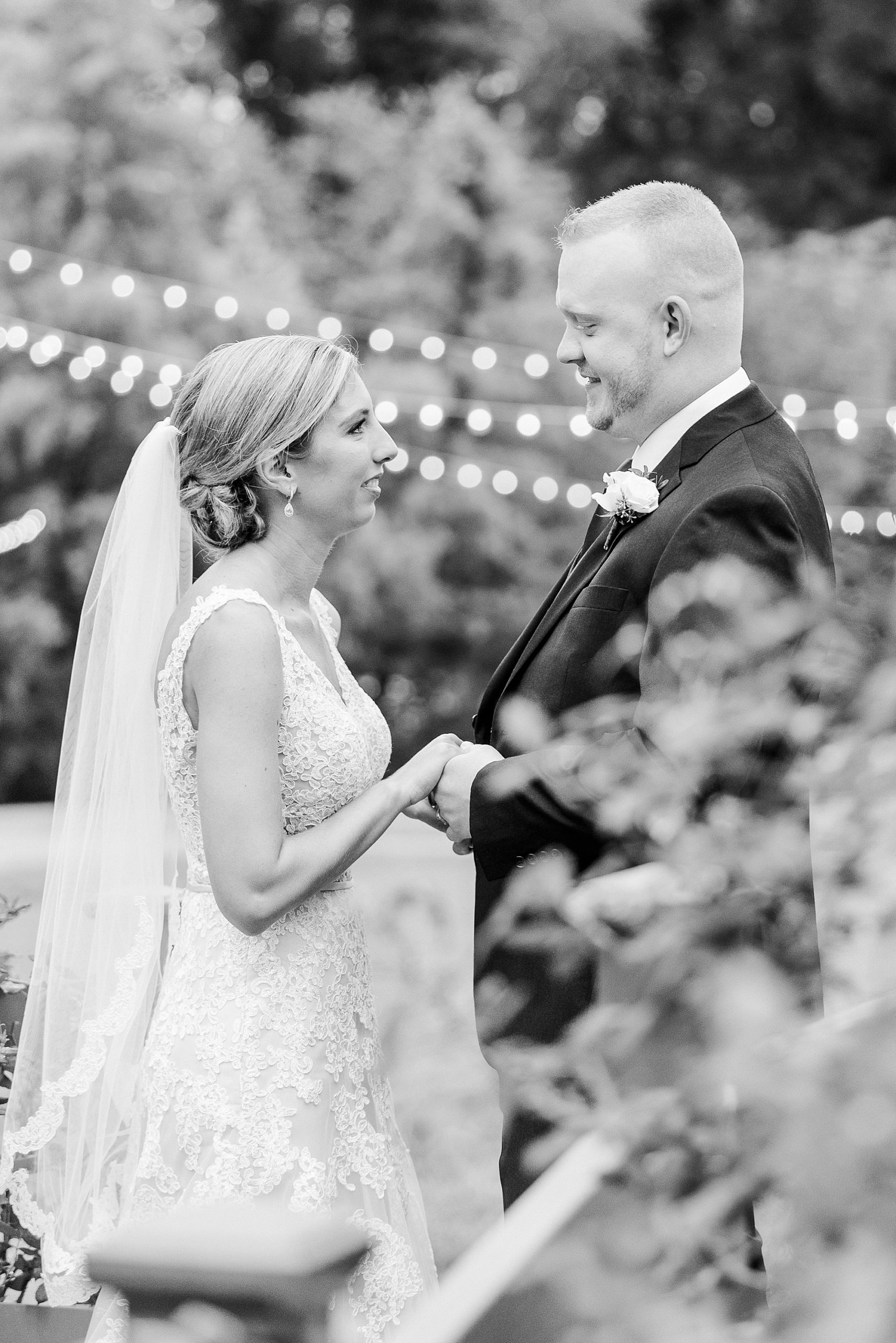 newlyweds hold hands standing by patio lights at Alexander Homestead