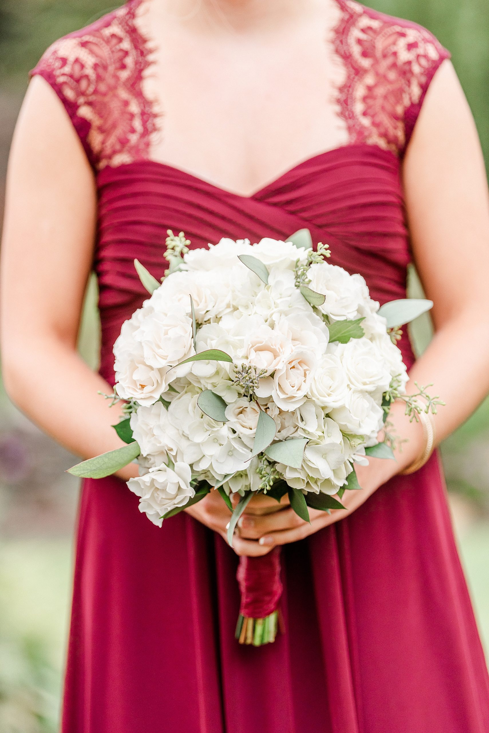 bride in burgundy dress holds all white bouquet