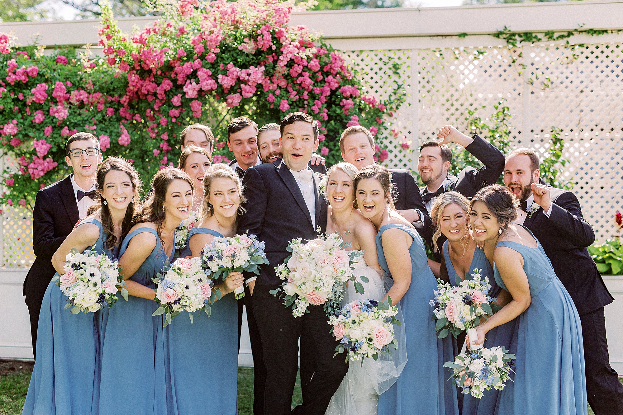 wedding party in blue and black laughs with bride and groom
