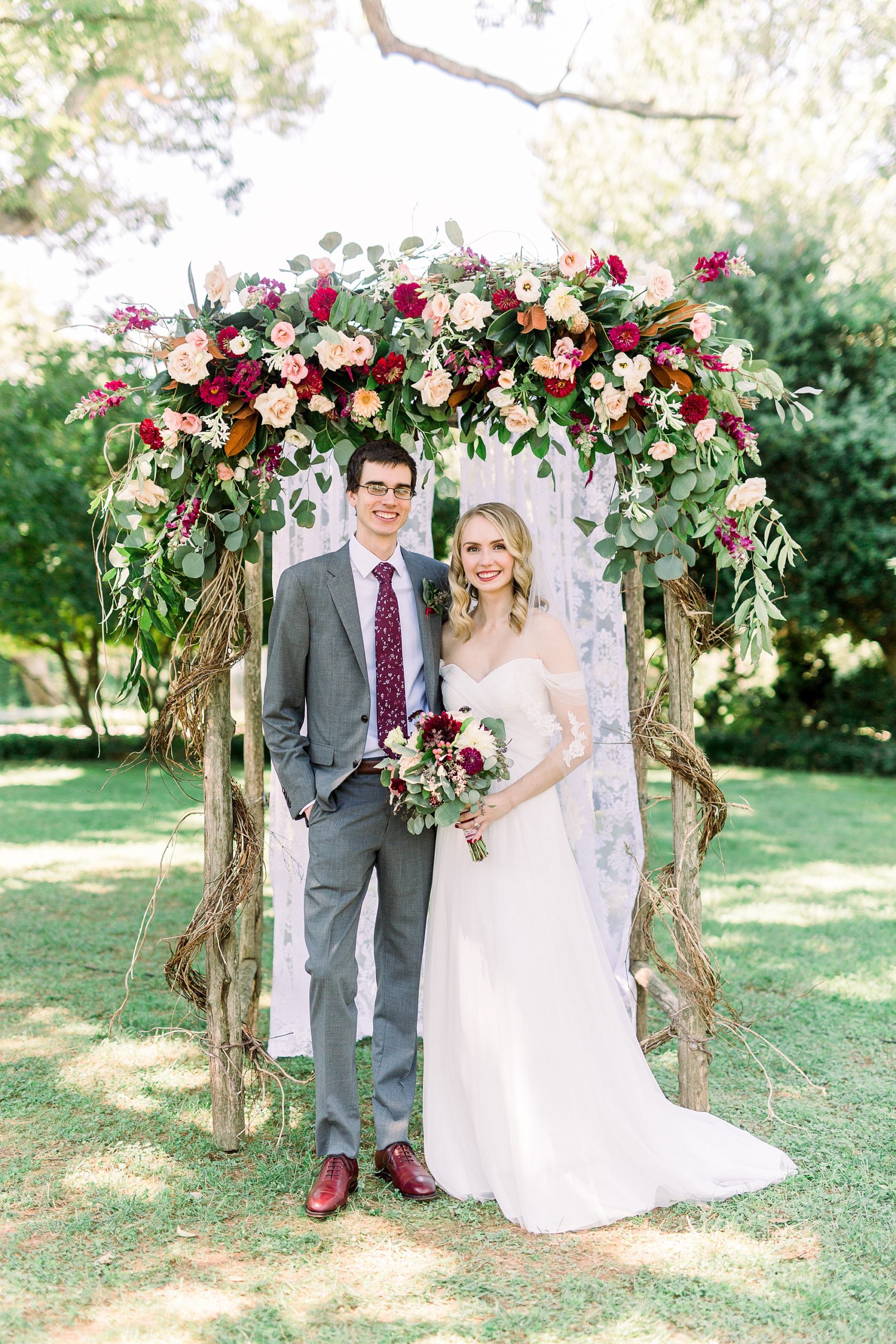 bride and groom pose under floral arbor at 1812 Hitching Post