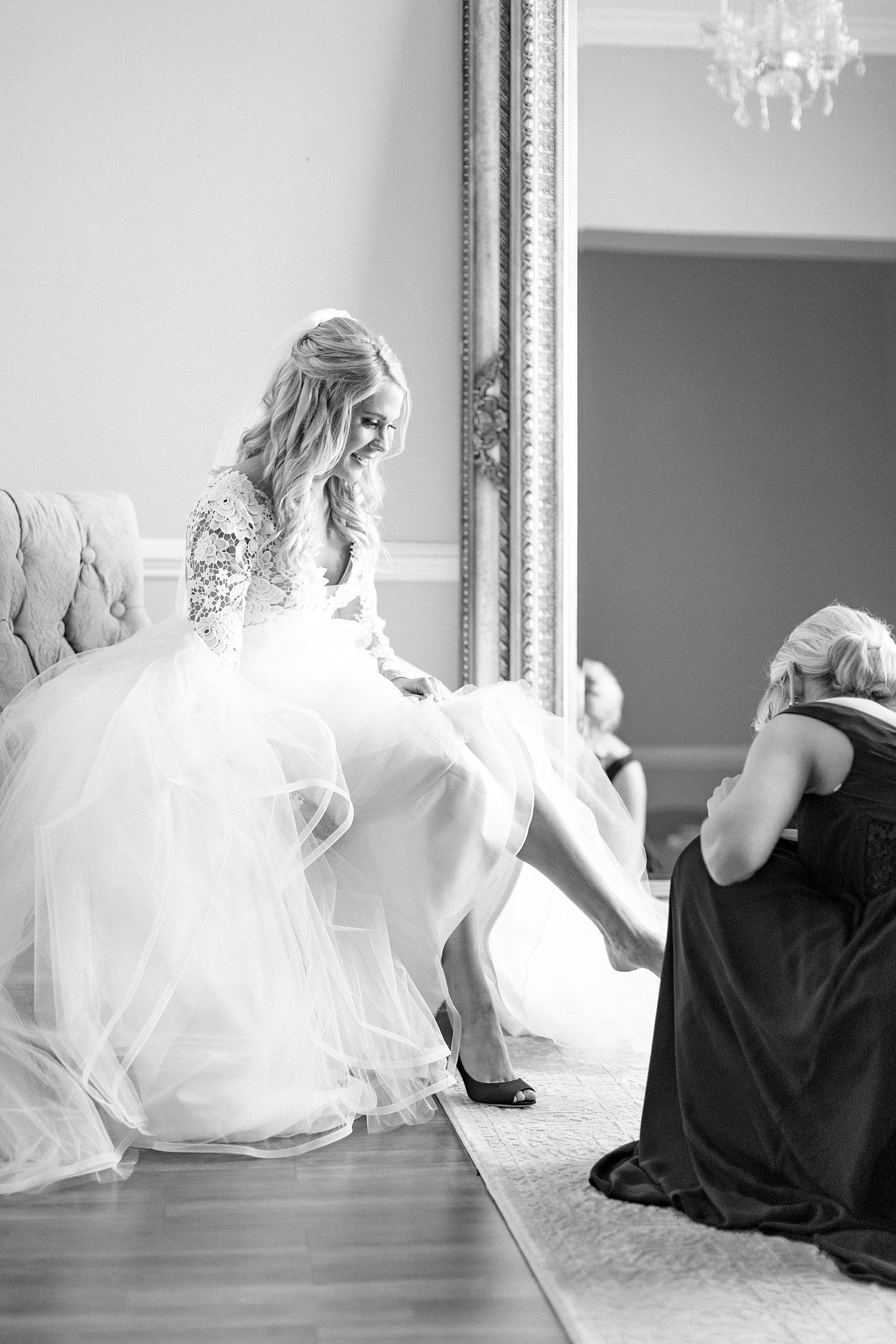 bridesmaid helps bride with heels under Hayden Olivia bridal gown