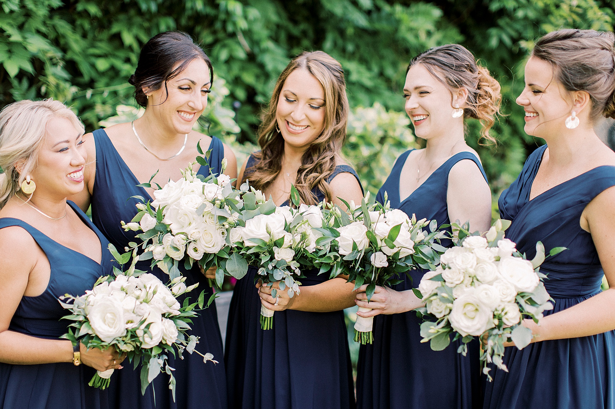 bride and bridesmaids in navy blue laugh holding white bouquets