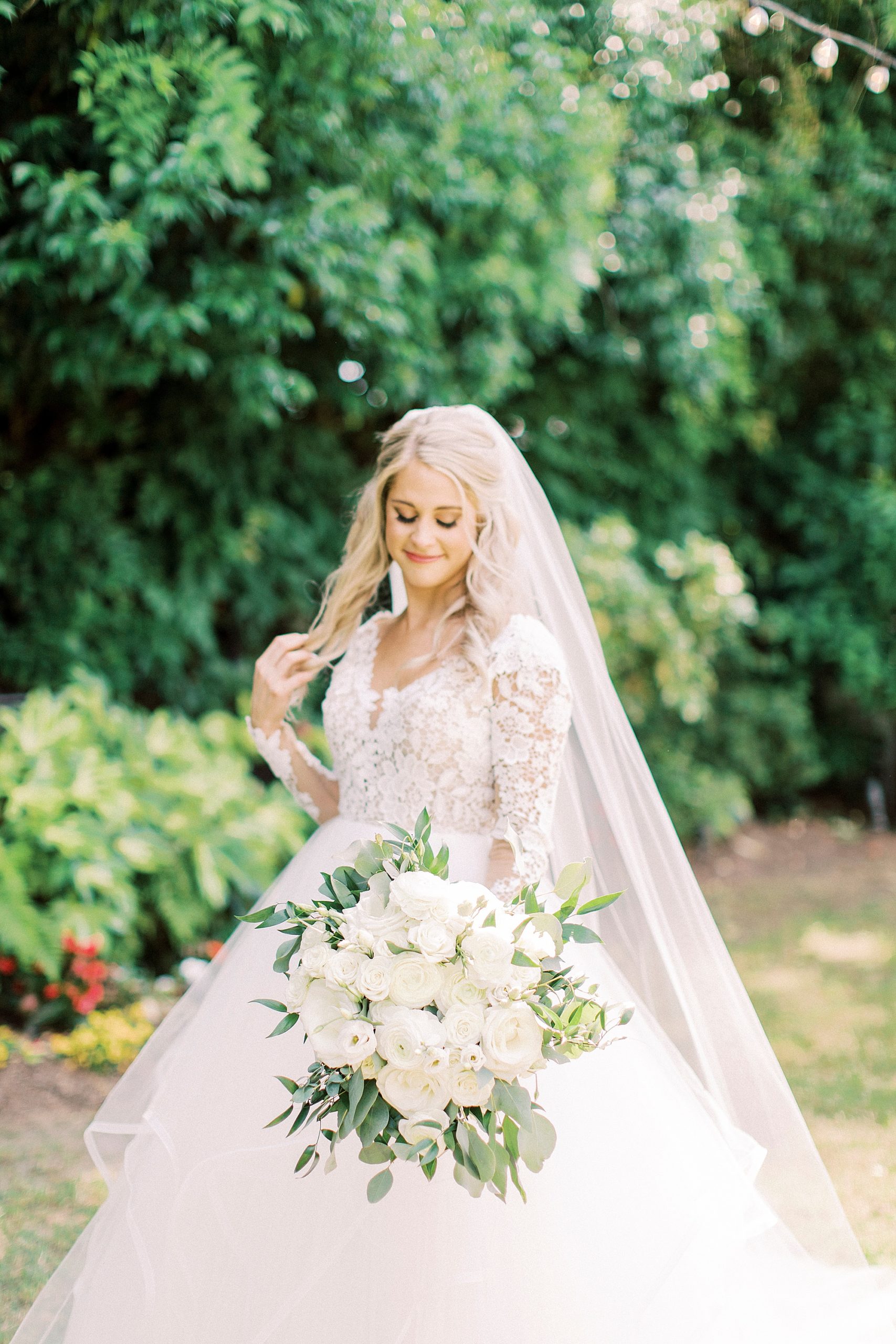 bride poses holding all-white bouquet looking down at flowers