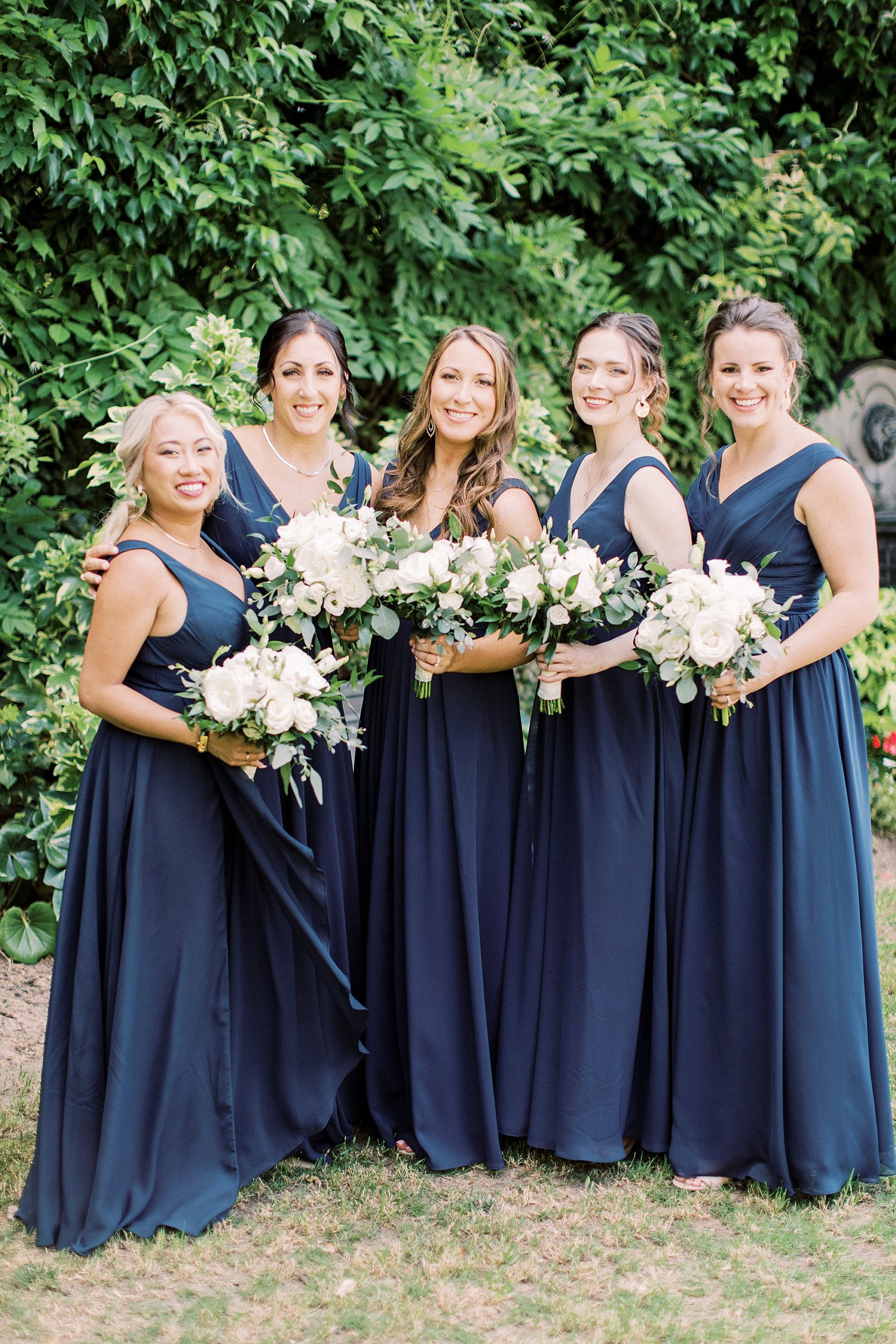 bridesmaids in navy blue hold white bouquets