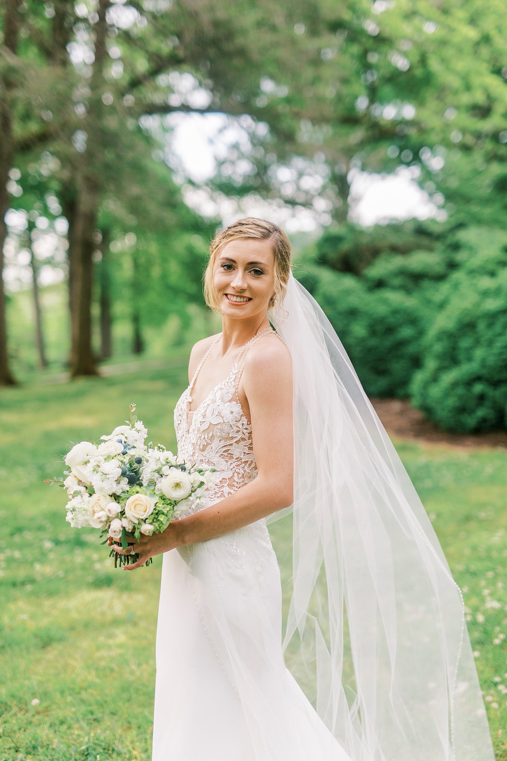 bride holds bouquet and looks over shoulder with veil draped