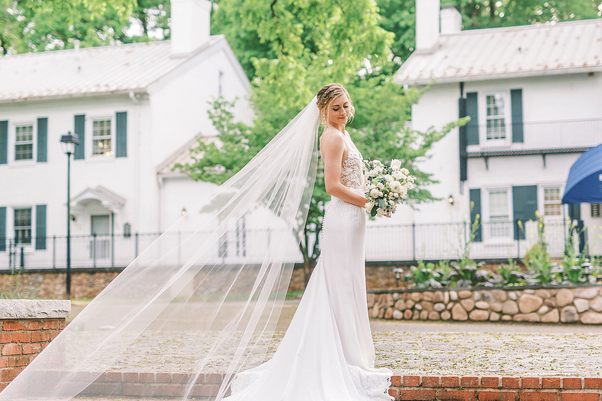 bride stands on steps with bouquet and veil draped behind her