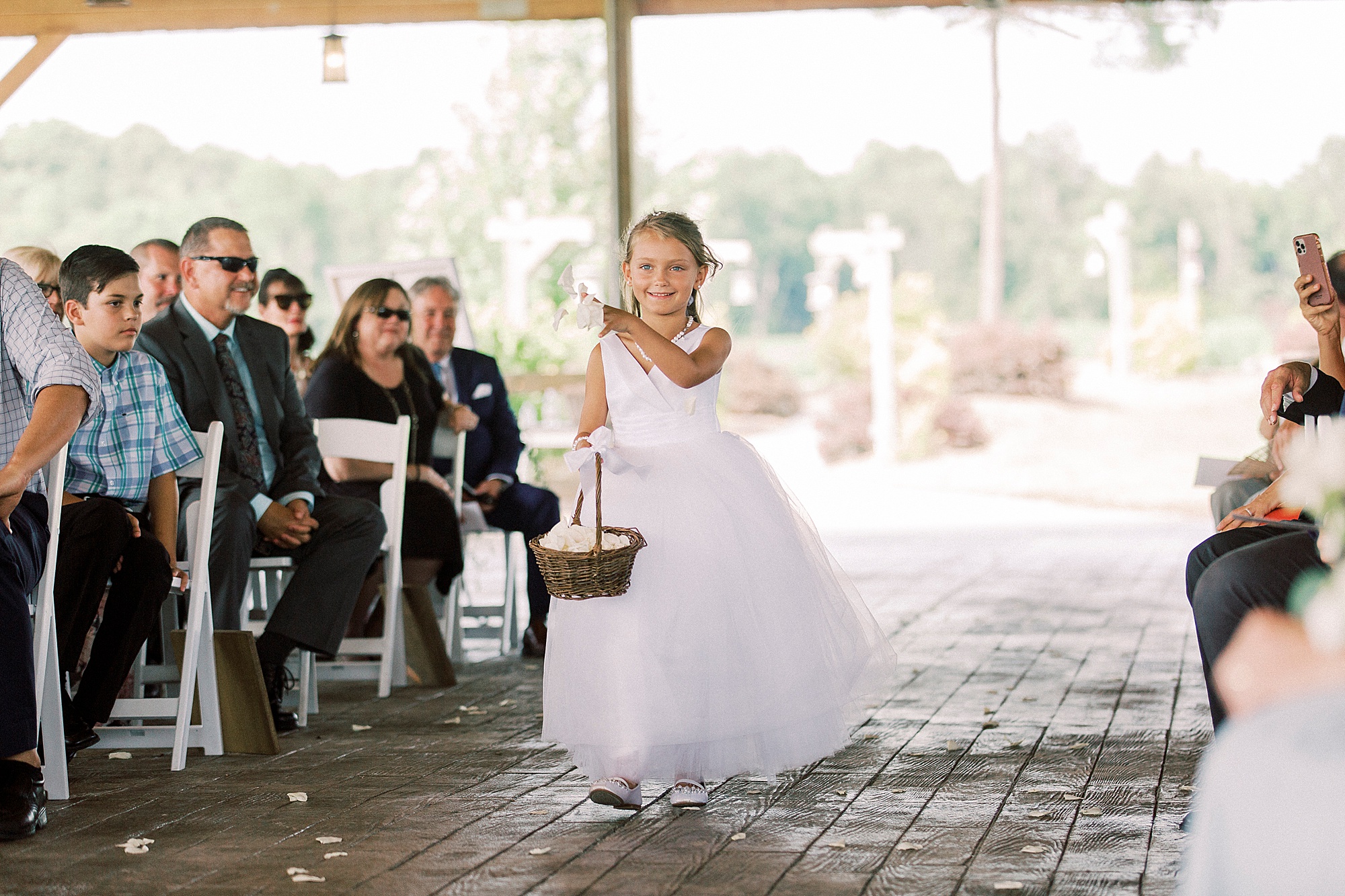flower girl walks down aisle at rustic wedding ceremony by wooden cross at The Farmstead