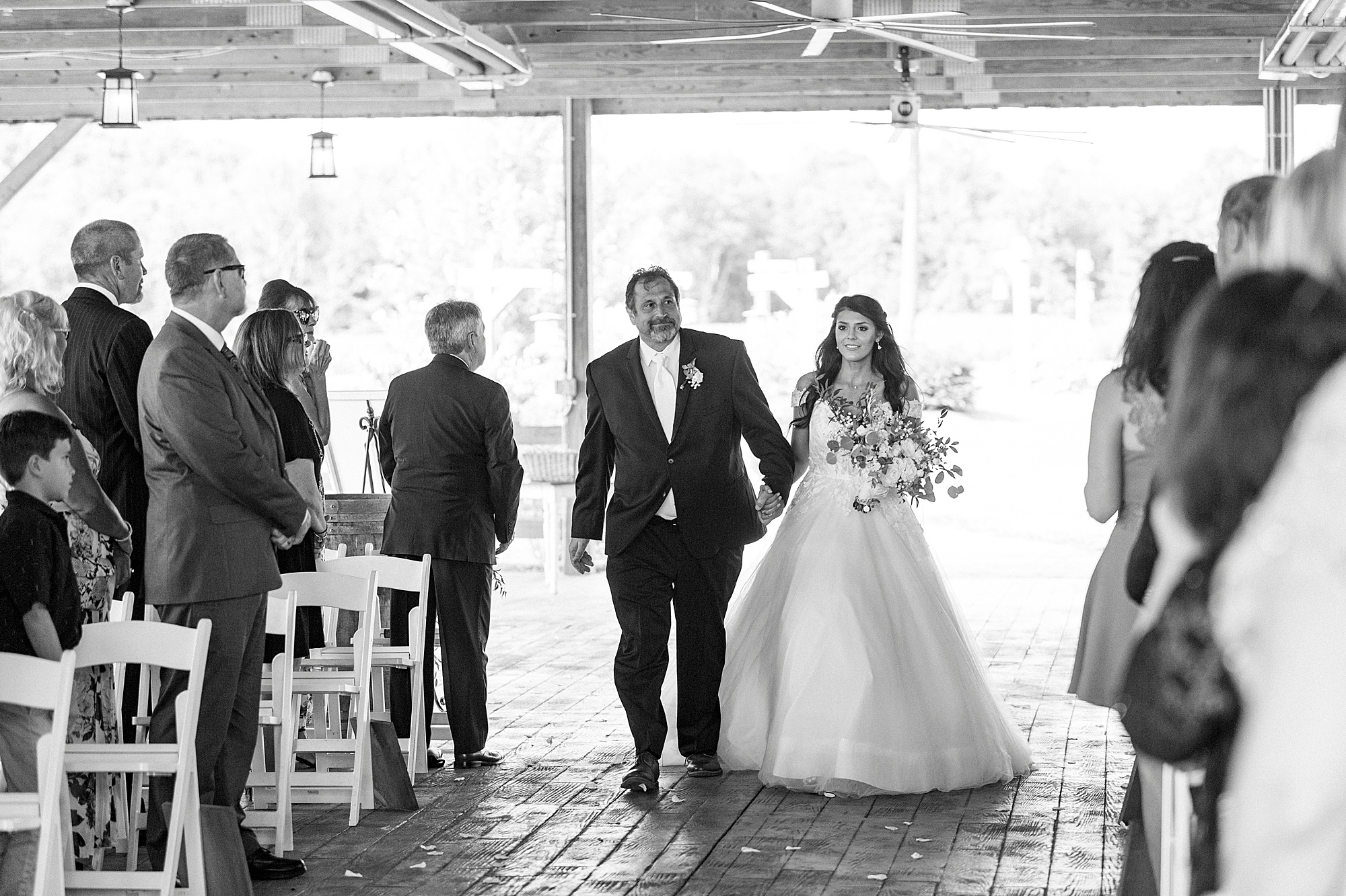 bride and dad enter rustic wedding ceremony by wooden cross at The Farmstead