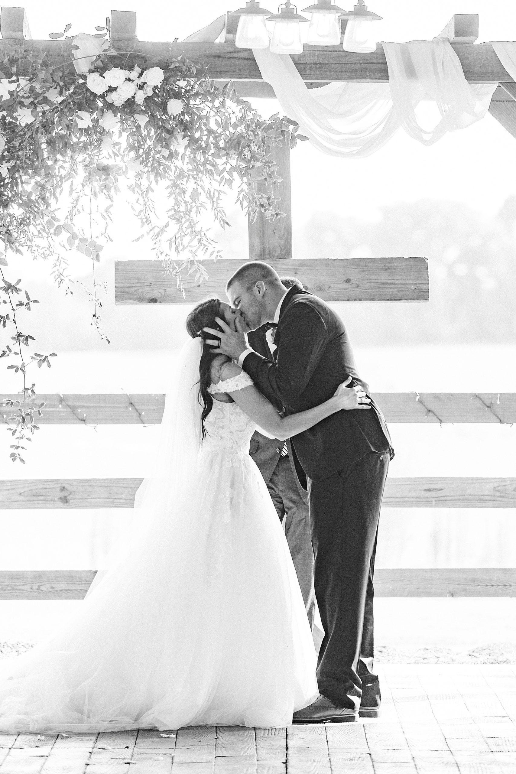 newlyweds kiss by wooden cross at The Farmstead