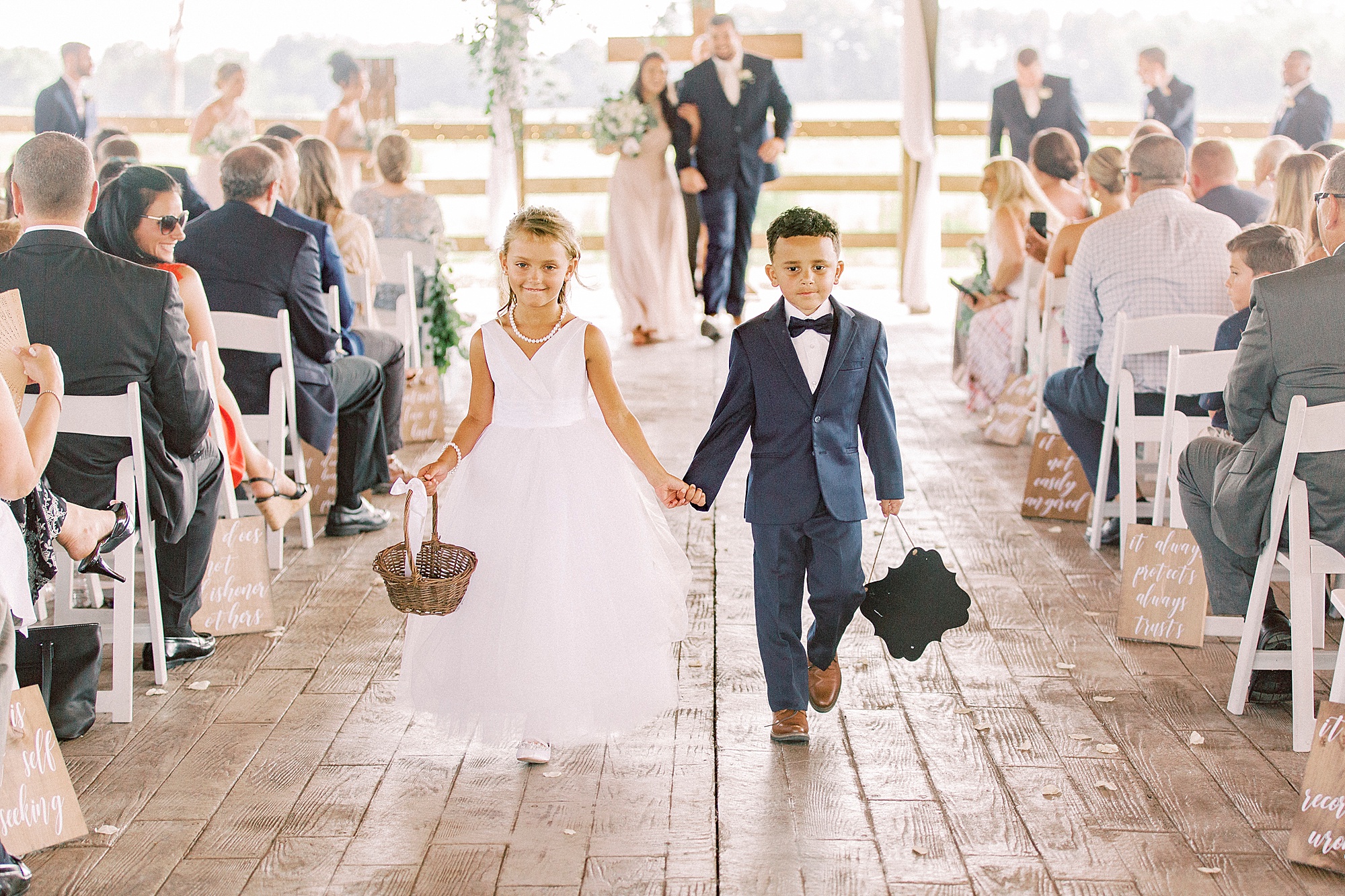 flower girl and ring bearer hold hands walking up aisle at The Farmstead
