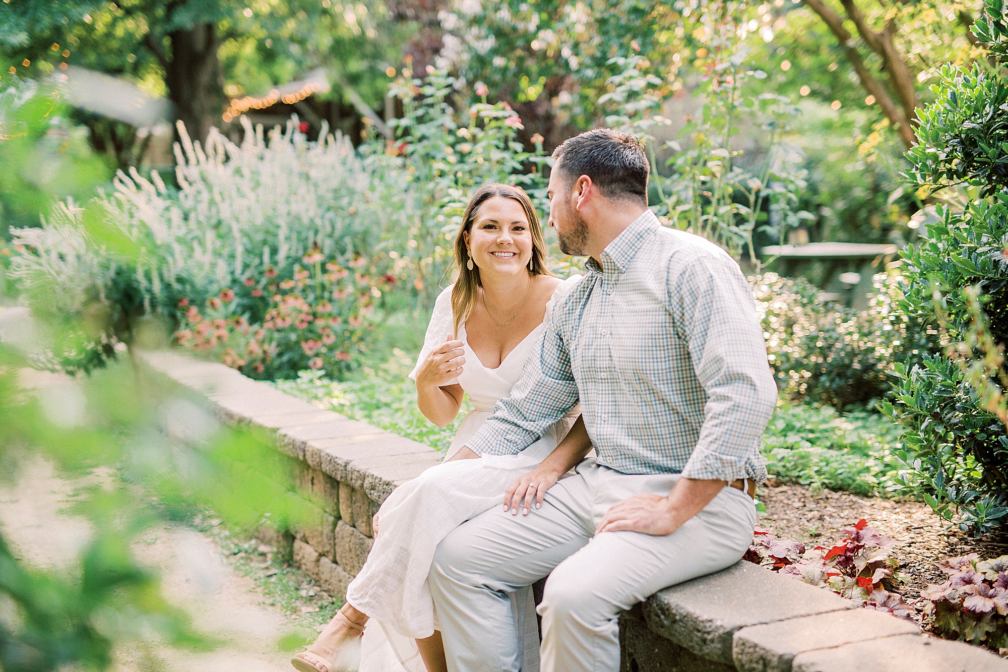 couple sits on brick wall in Charlotte garden