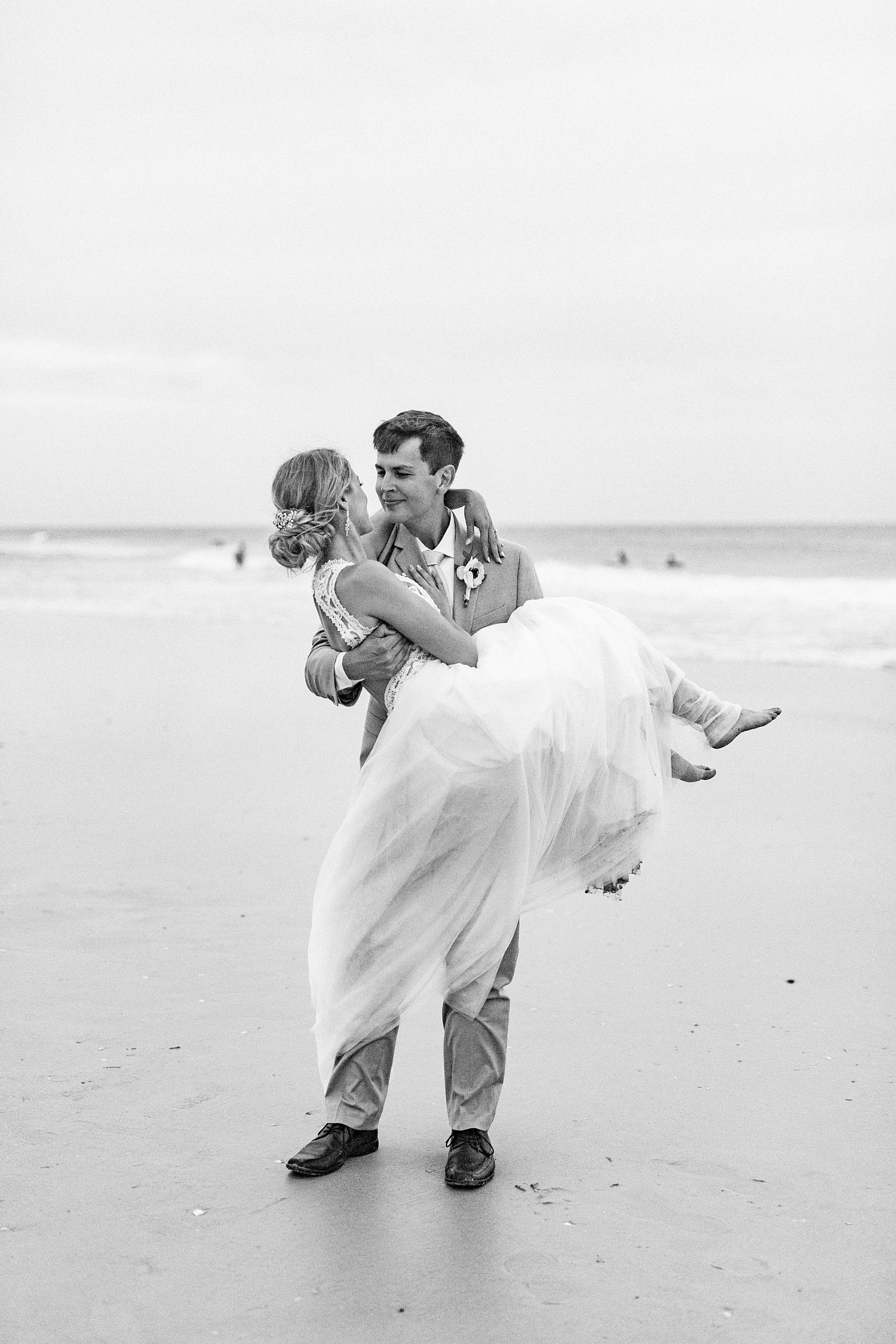 groom lifts bride up during wedding portraits on the beach