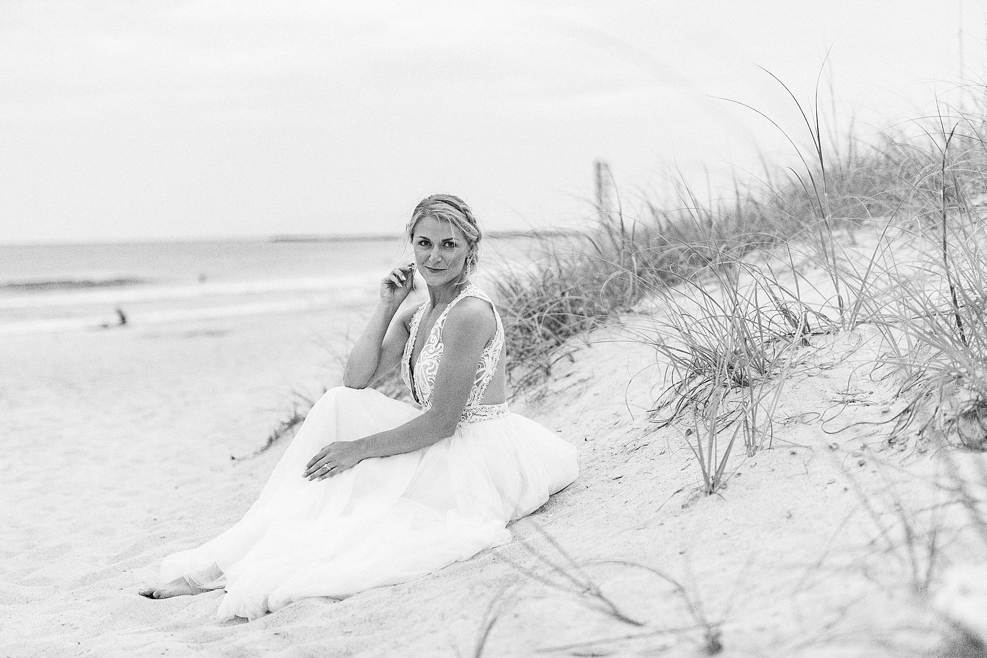 bride sits on sand dune at Wrightsville Beach