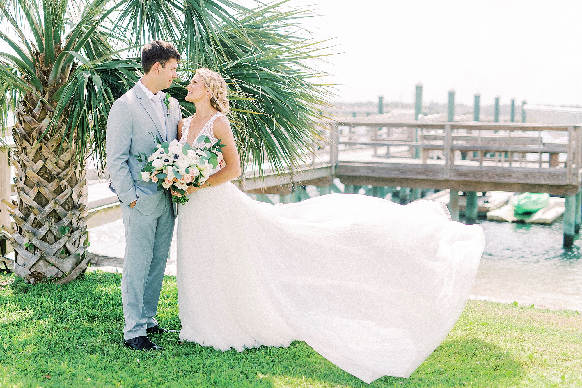 newlyweds pose by palm tree with bride's dress bowing in wind
