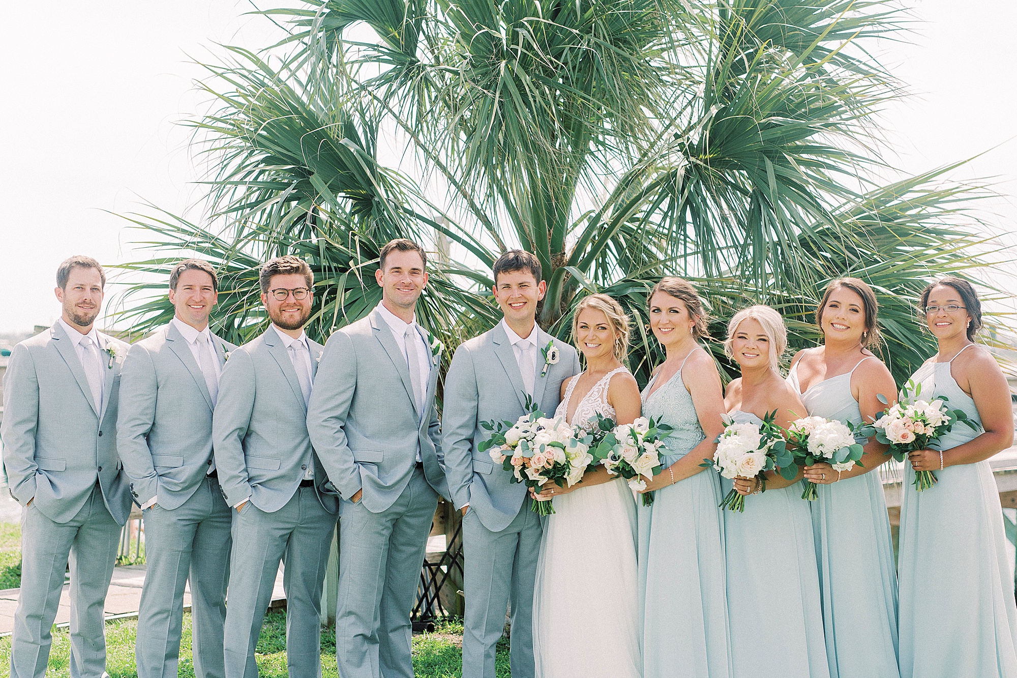 newlyweds pose with wedding party in light grey and blue