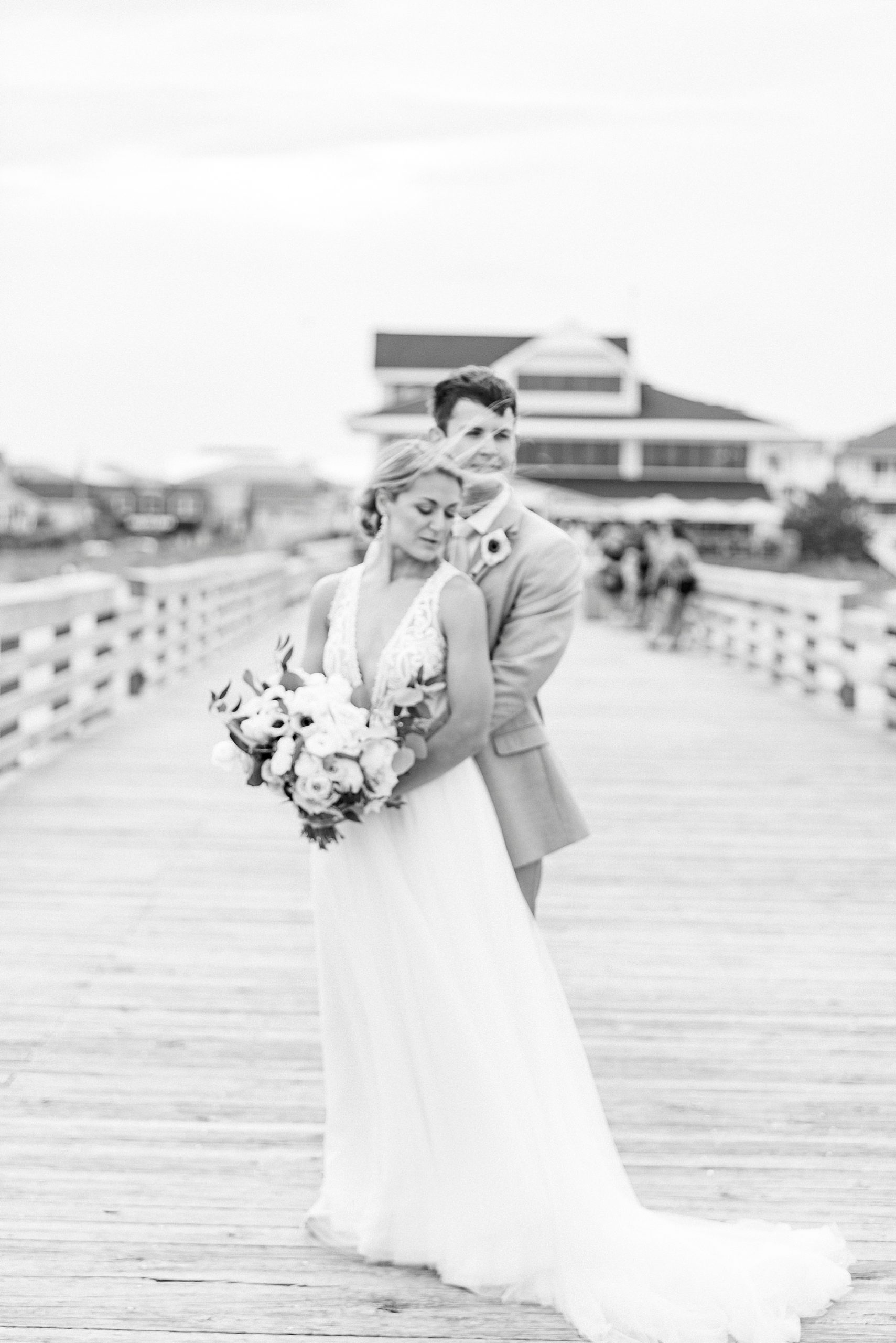 groom hugs bride on pier at Wrightsville Beach