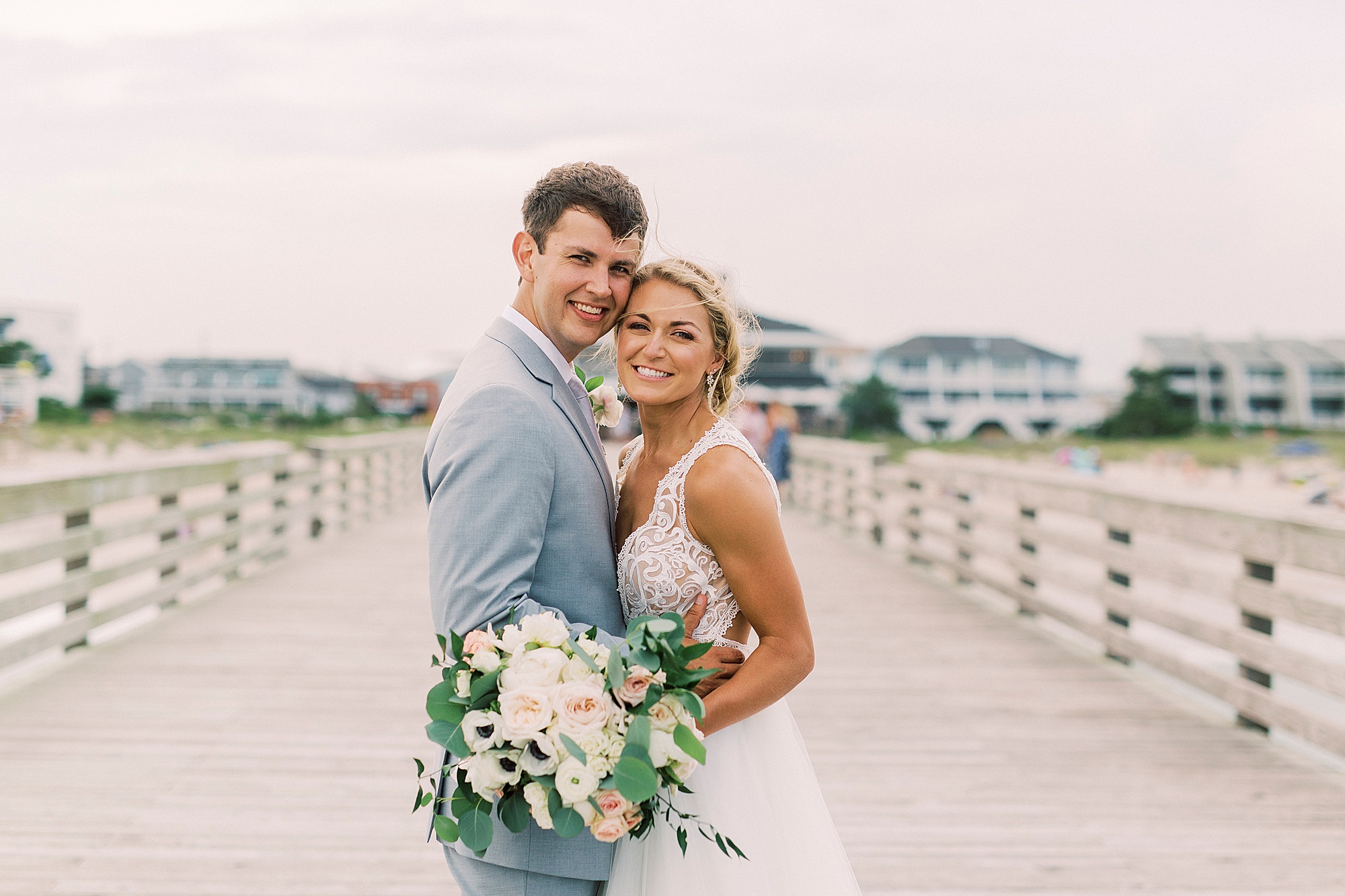 newlyweds hug on pier at Wrightsville Beach