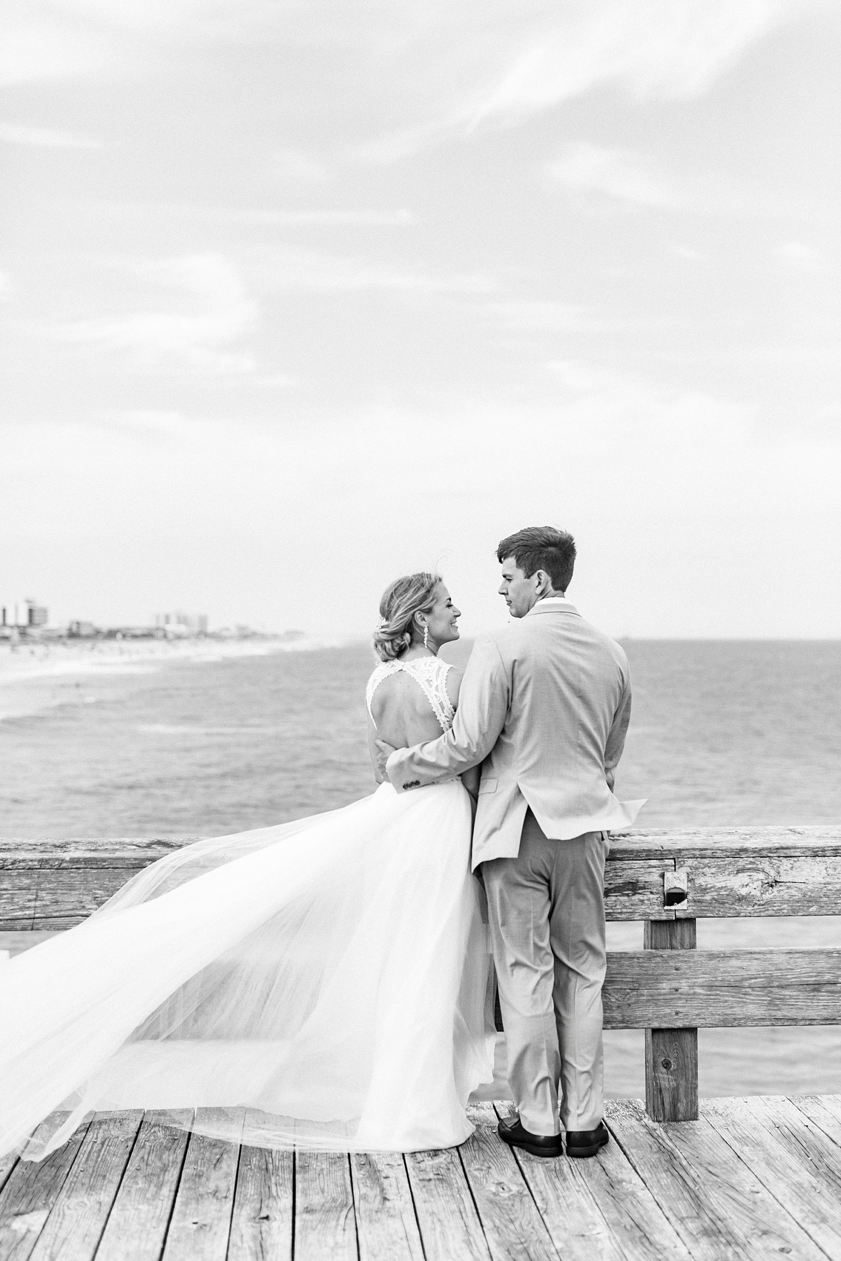 bride and groom smile at each other standing on wooden pier